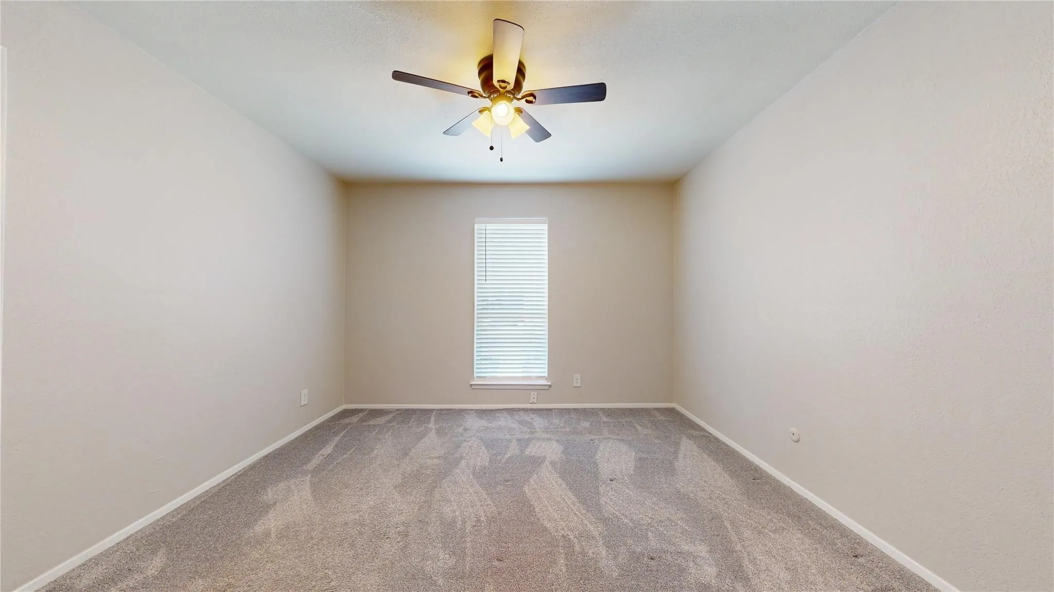 Neutral wall paint, ceiling fan with light fixture, window with blinds, and patterned carpet flooring