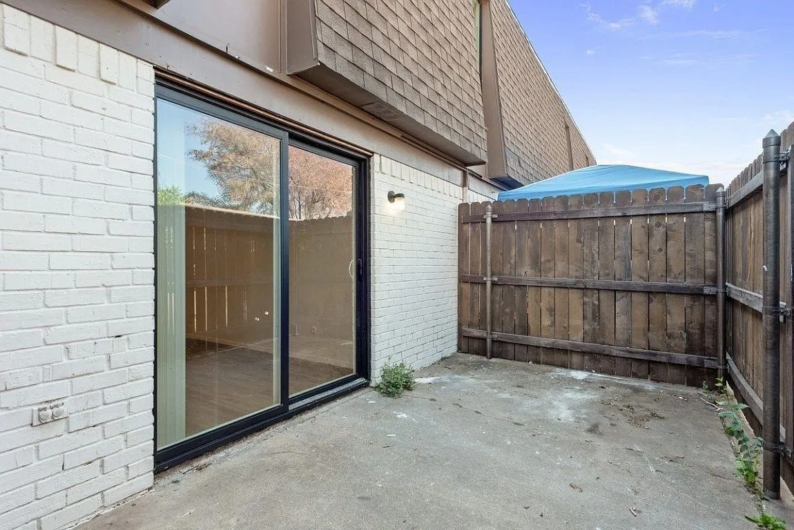 Private patio with concrete surfacing, white brick exterior, black-framed sliding glass door, and wood privacy fencing