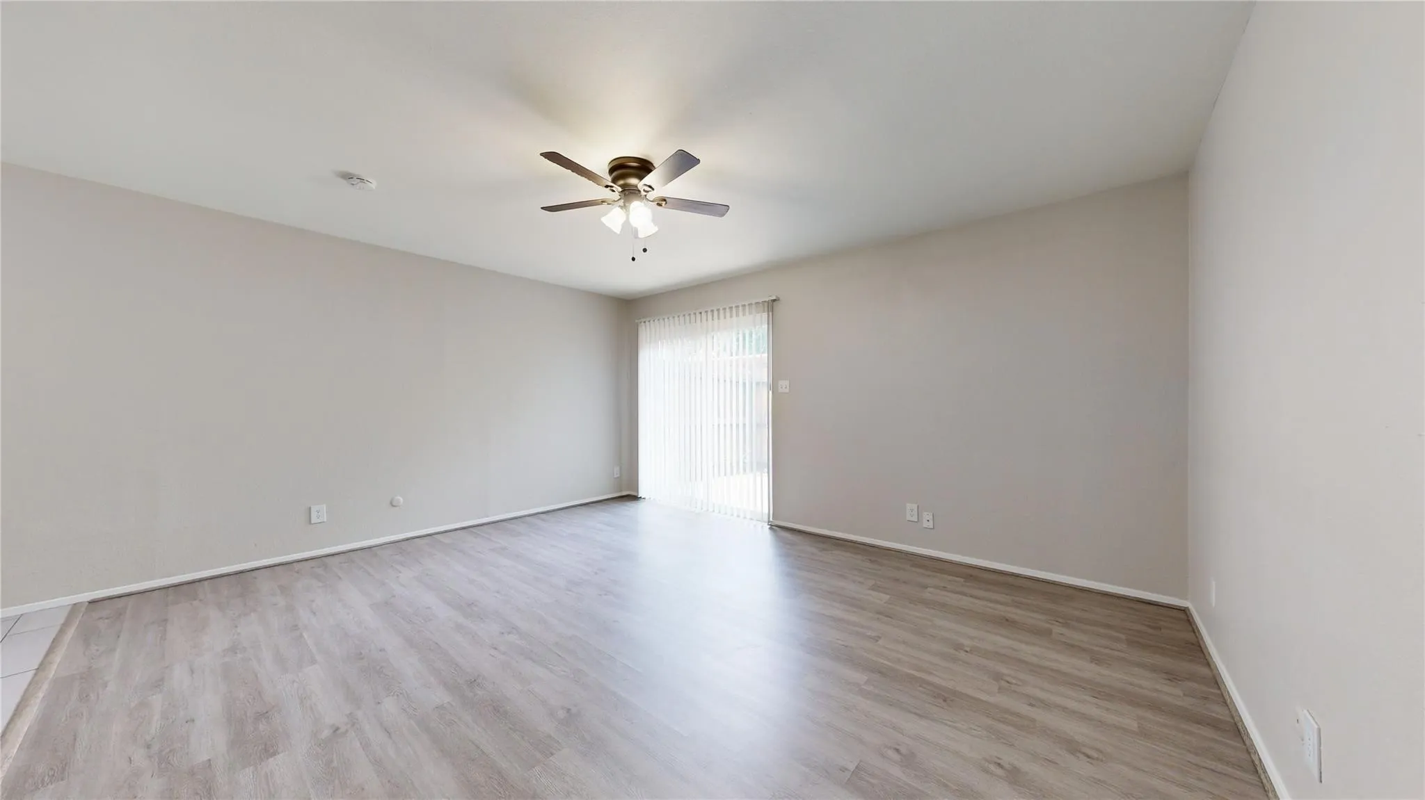 Spacious room featuring wood-finish flooring, light-toned walls, and a ceiling fan with integrated lighting