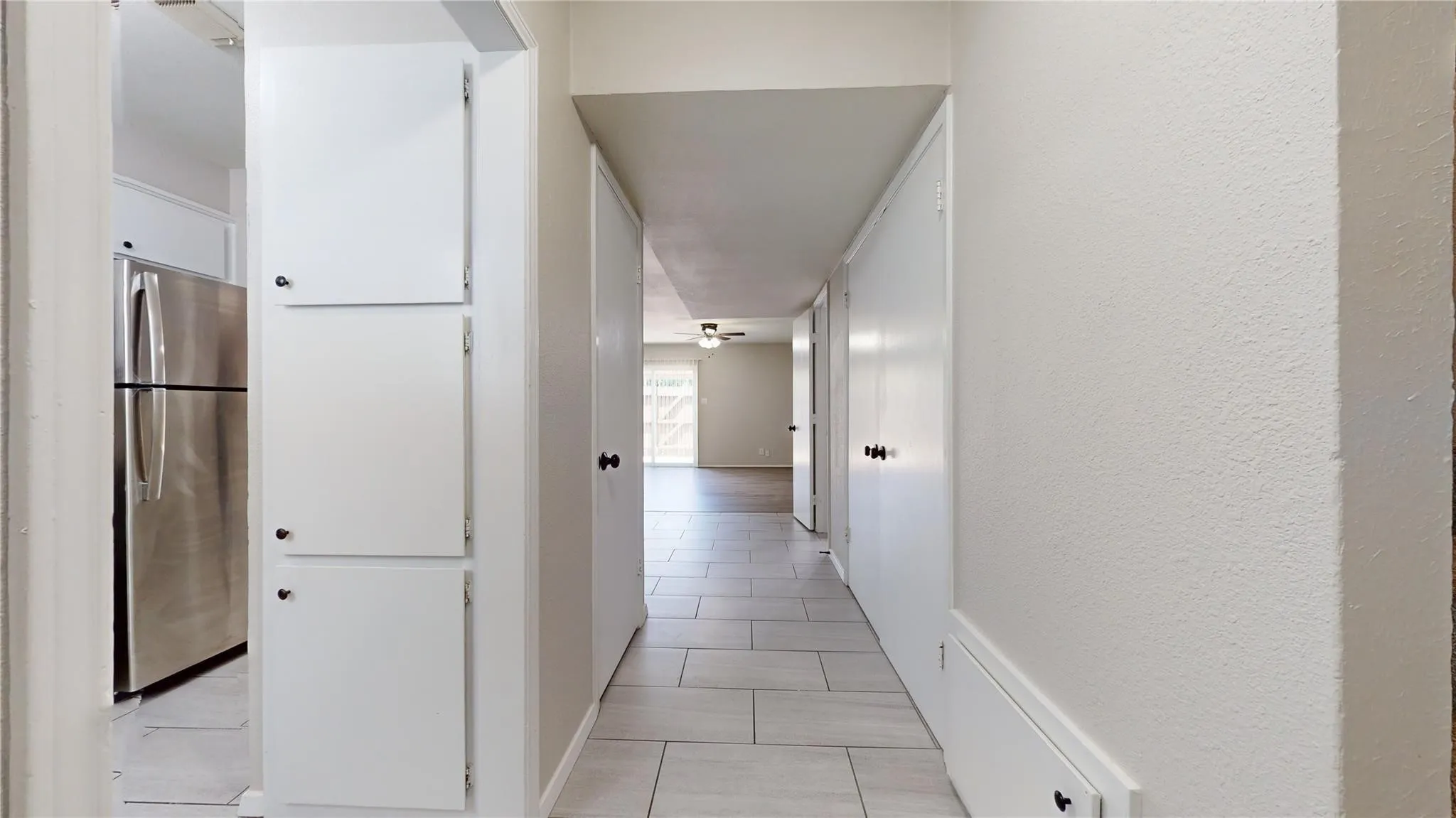 Galley-style hallway featuring tiled flooring, built-in storage cabinetry, and a refrigerator with a stainless steel finish