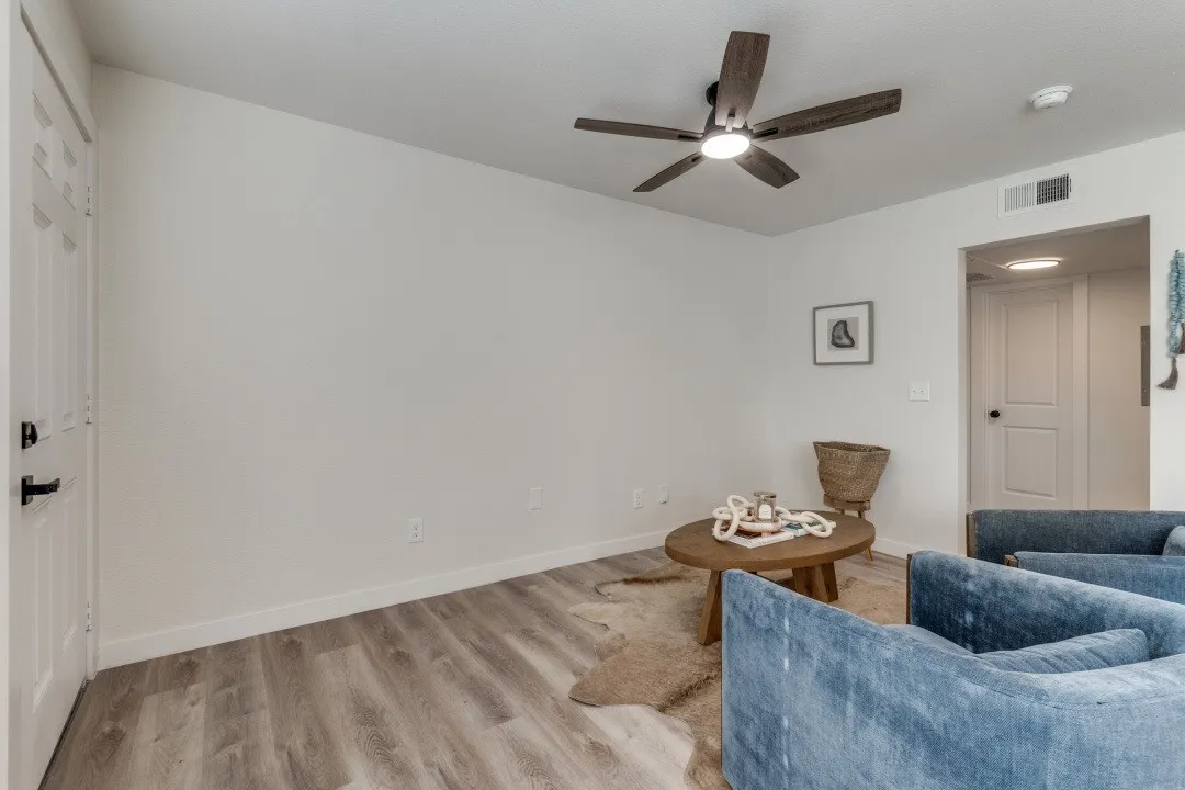 Wood-finish flooring, white paneled door with black hardware, and a ceiling fan with light fixture
