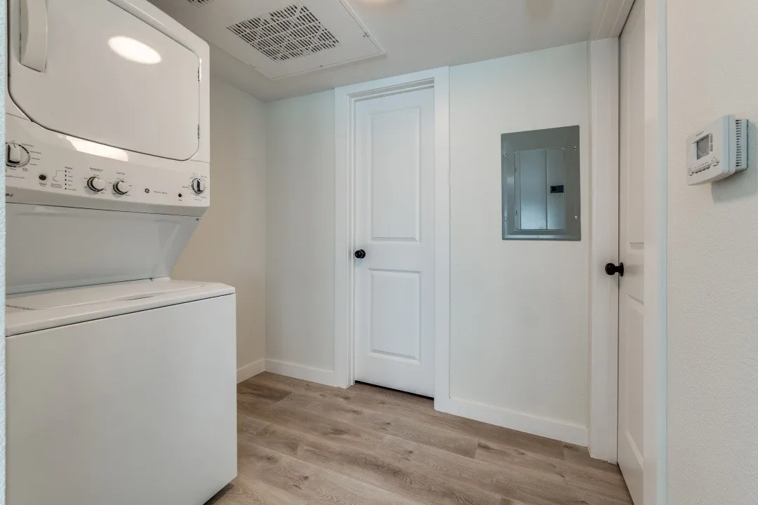 Stackable laundry appliances, wood-finish flooring, white walls, white doors, and a ceiling-mounted light fixture