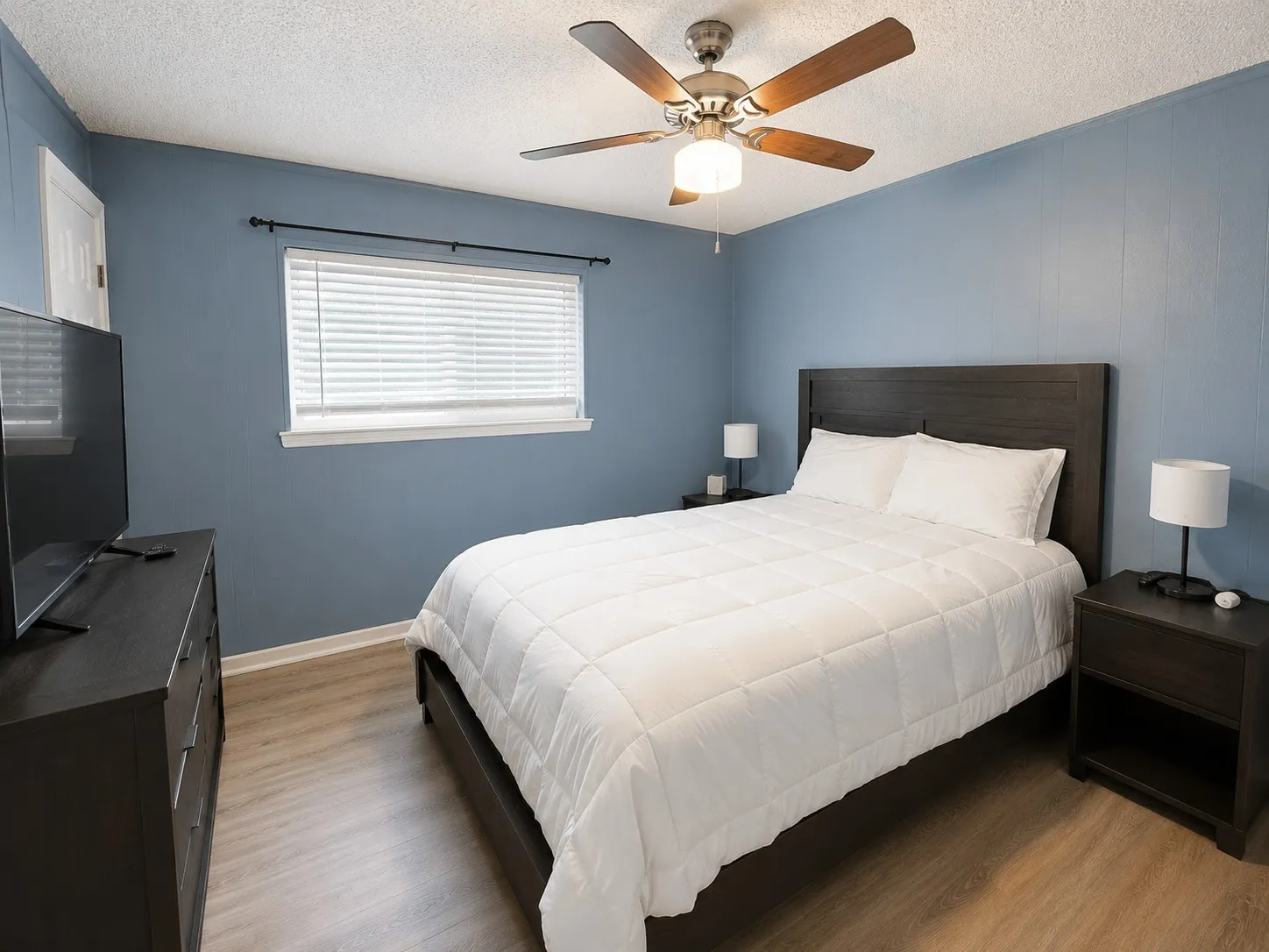 Wood-finish flooring, ceiling fan with integrated lighting, window with blinds, and paneled walls