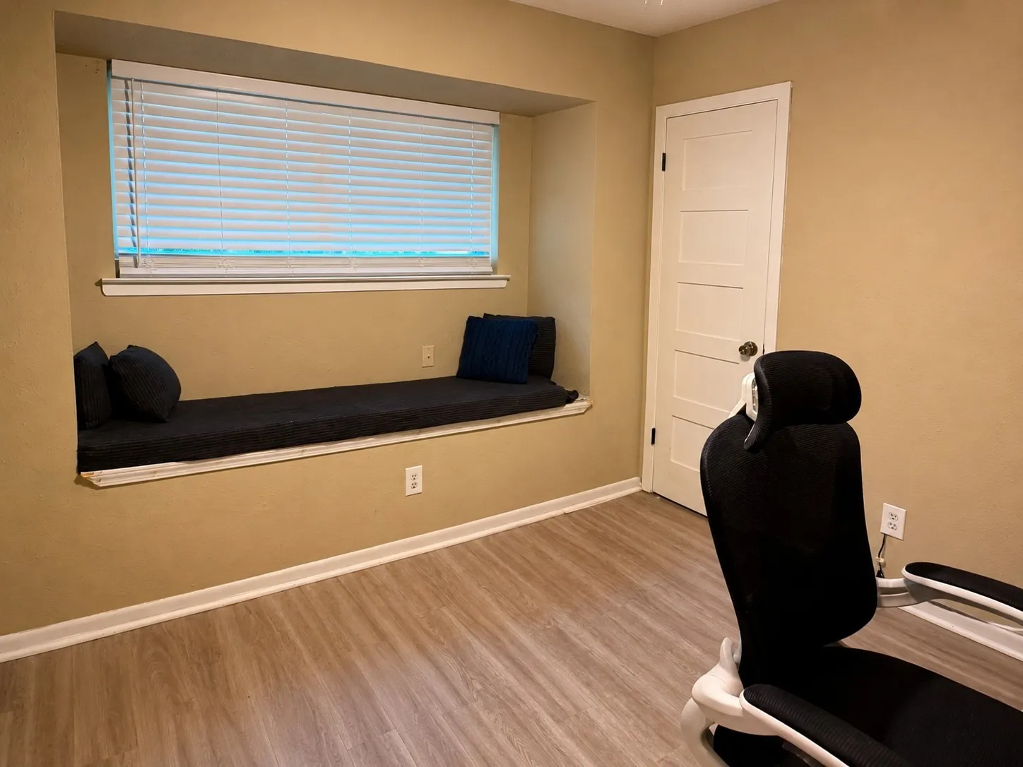 Built-in window seat, large window with blinds, wood-finish flooring, white trim, and a paneled interior door