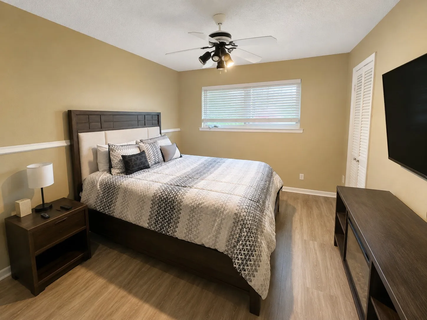 Wood-finish flooring, ceiling fan with integrated lighting, window with blinds, and louvered bi-fold door