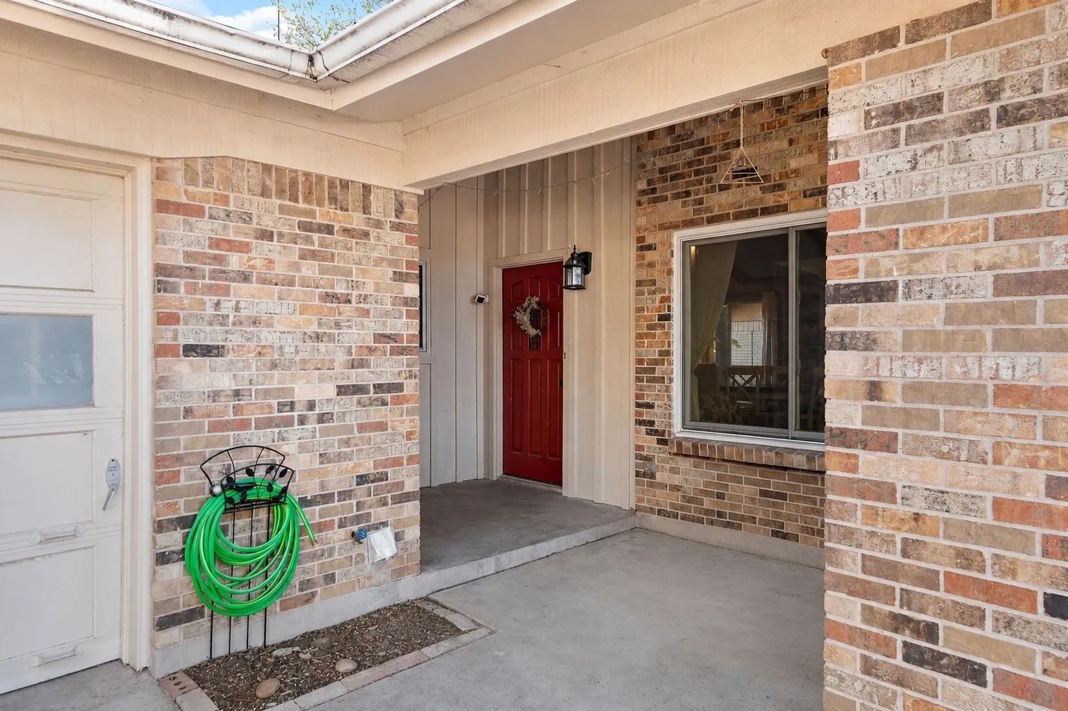 Brick exterior with a red entry door, covered entry, and an attached garage featuring translucent window panels