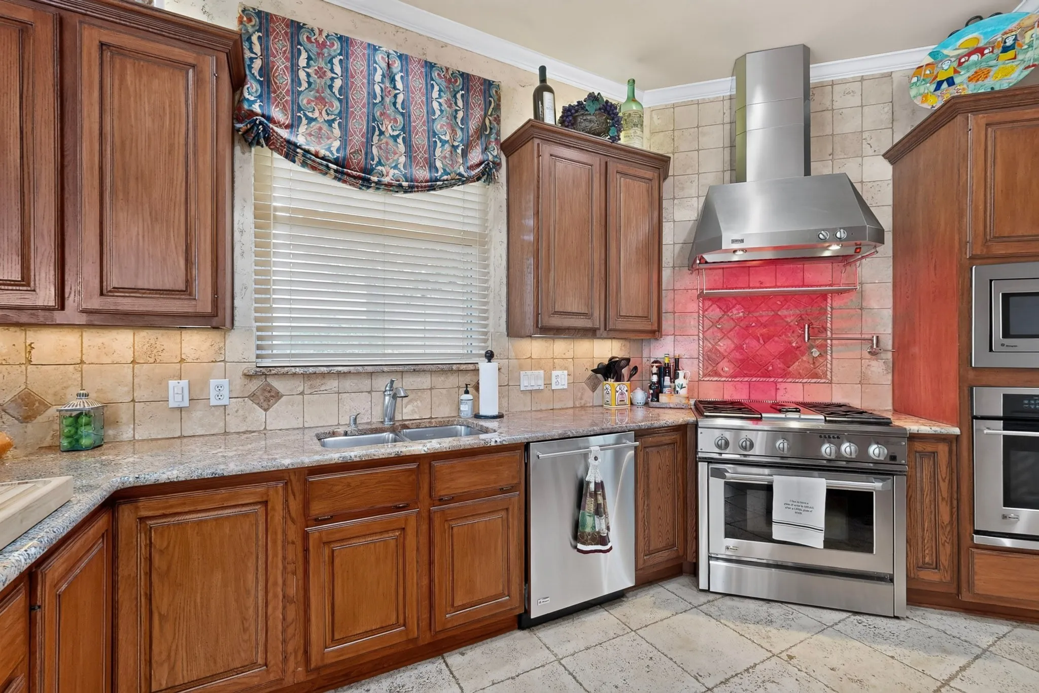 Wood cabinetry, light-toned tiled backsplash, granite-style countertops, stainless steel appliances, and tiled flooring