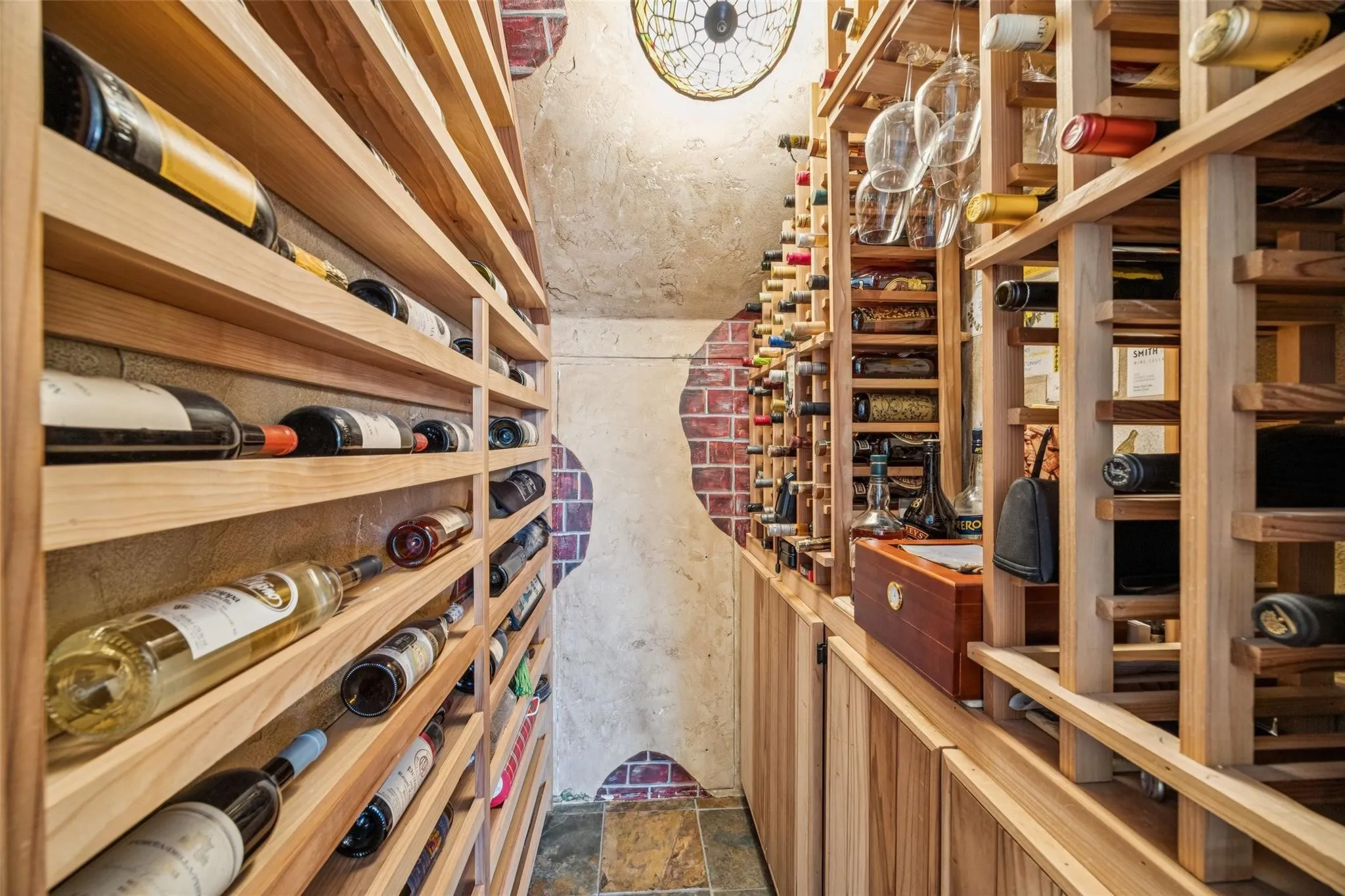 Dedicated wine cellar with extensive wood bottle shelving, integrated storage cabinets, and a unique brick and stucco wall treatment