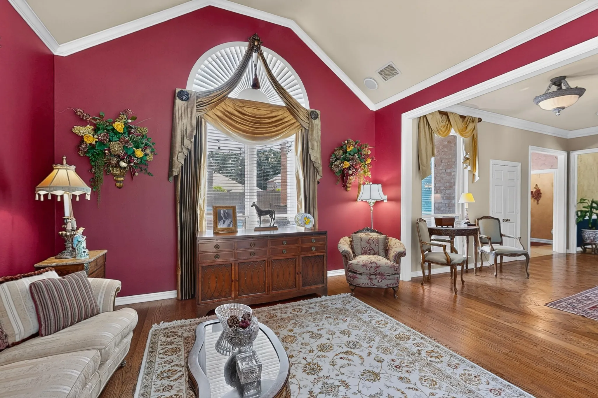 Vaulted ceiling with crown molding, arched window with plantation shutters, wood-finish flooring, built-in cabinetry, and recessed lighting
