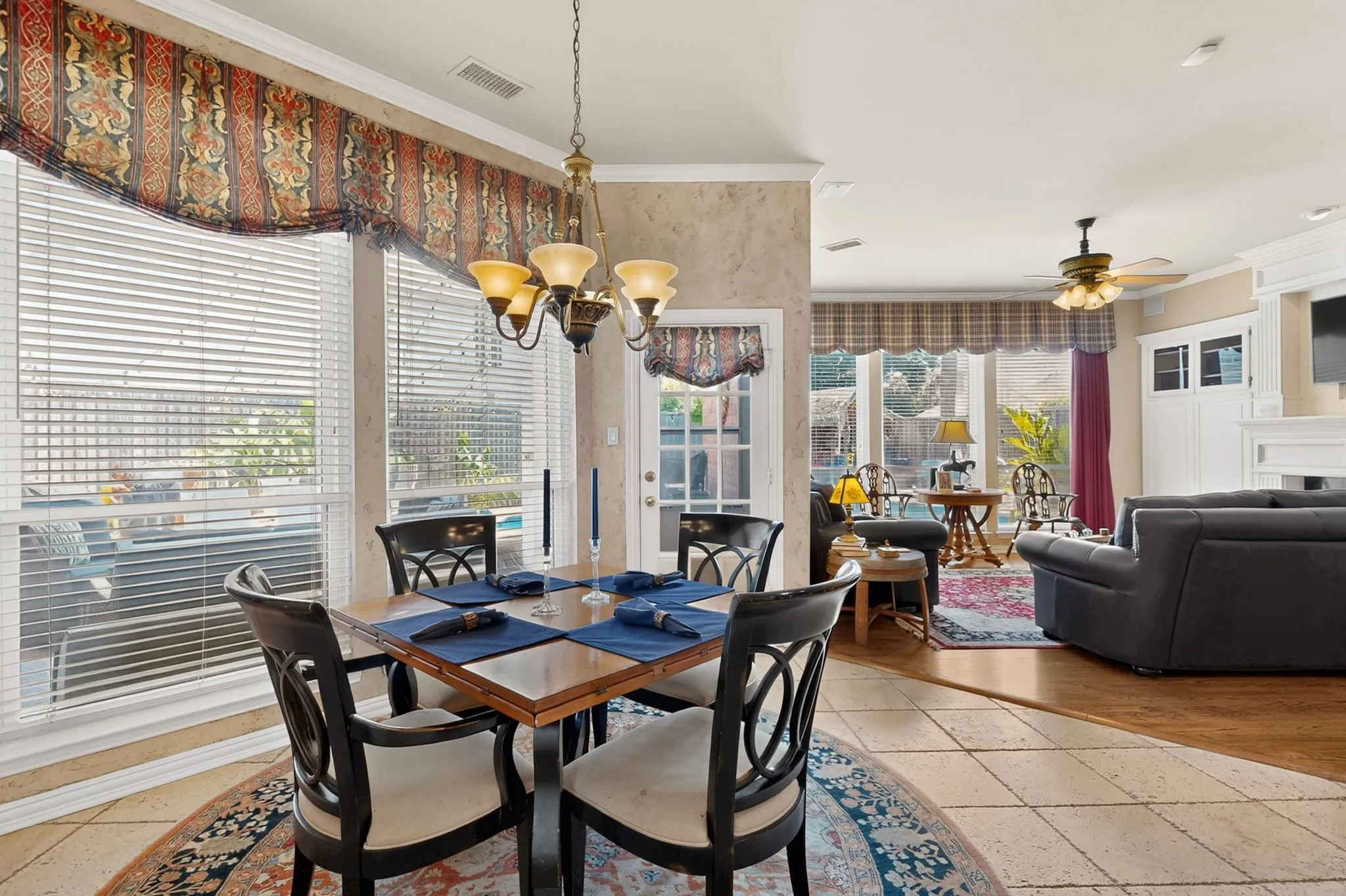 Tile flooring in the dining area with a brass chandelier, large windows with white blinds, and a built-in white media cabinet in the background