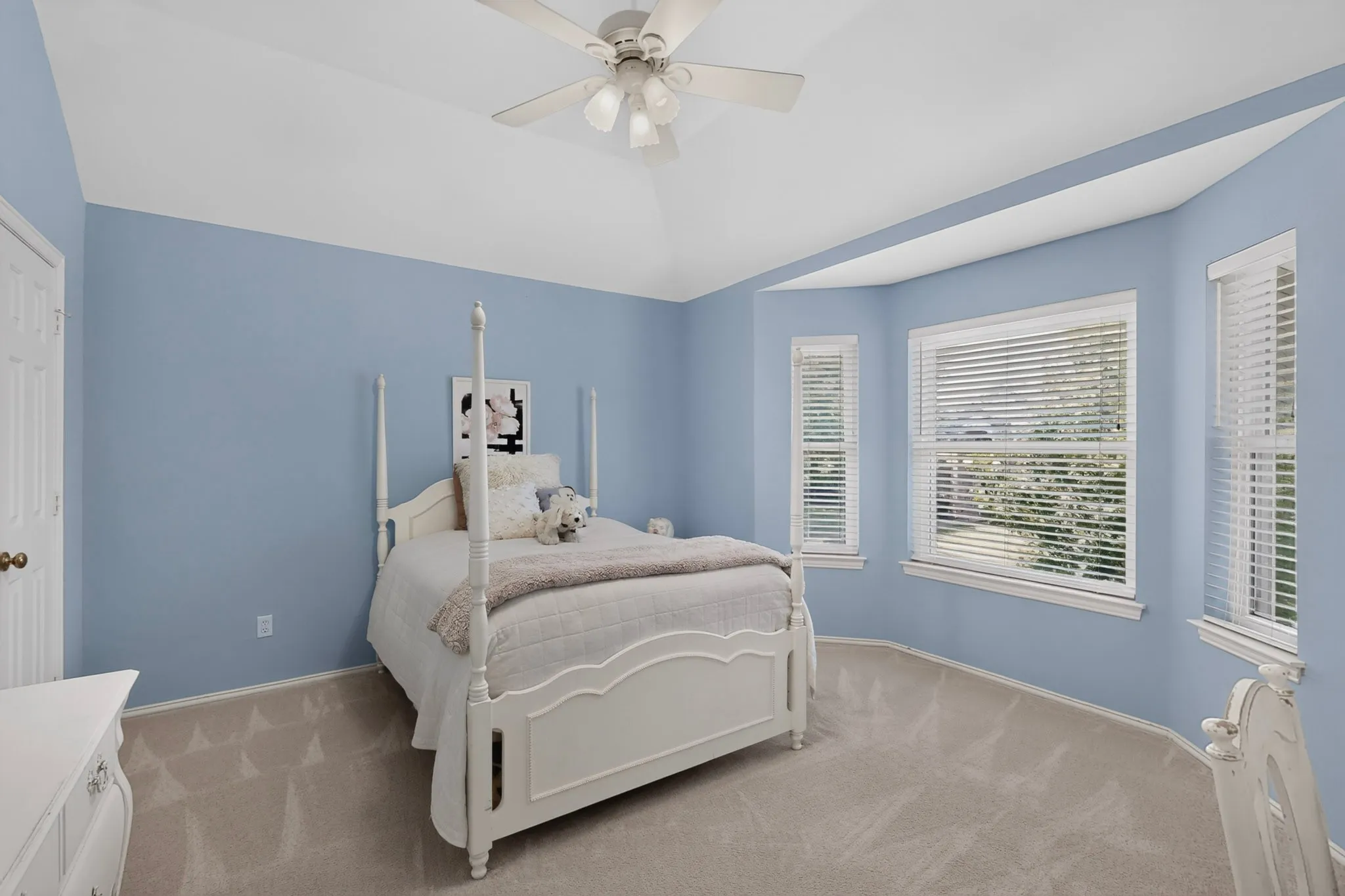 Vaulted ceiling with ceiling fan, bay window with multiple windows, light blue wall paint, paneled interior door, and carpet flooring