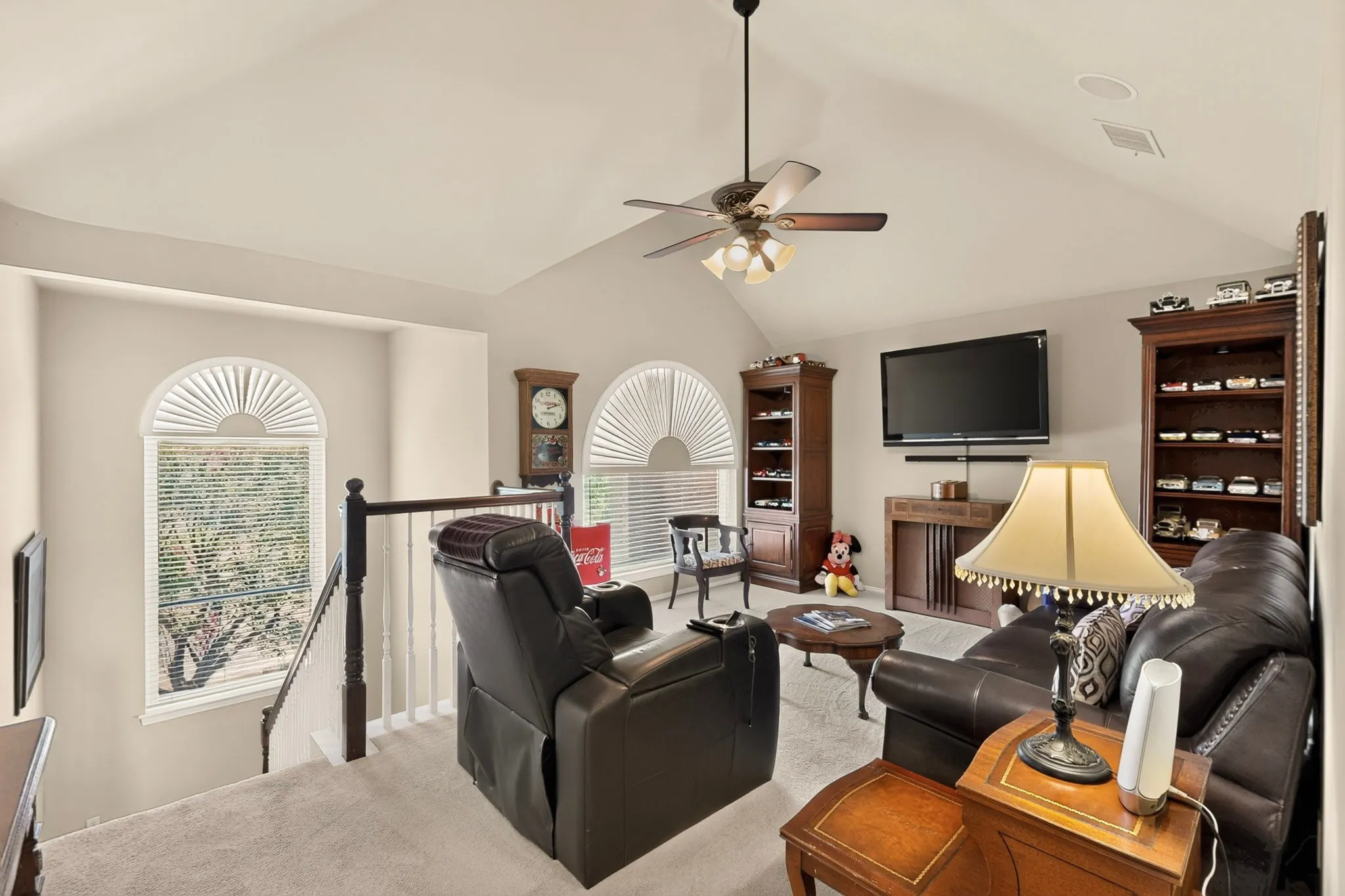 Vaulted ceiling with a ceiling fan, dual arched windows, built-in shelving, and carpeted flooring