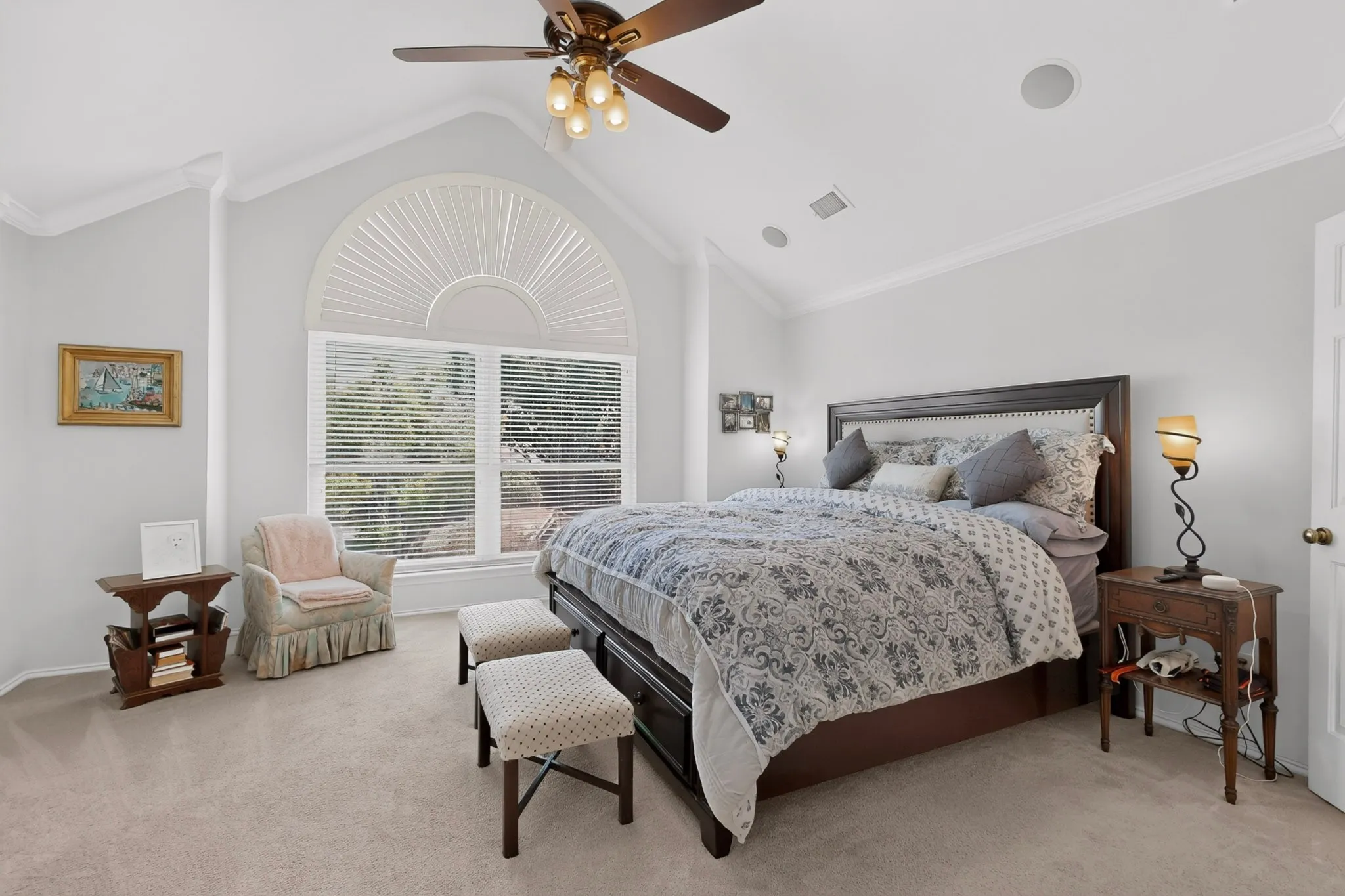 Vaulted ceiling with crown molding, ceiling fan with integrated lighting, arched window with horizontal blinds, carpeted flooring, and built-in ceiling speakers