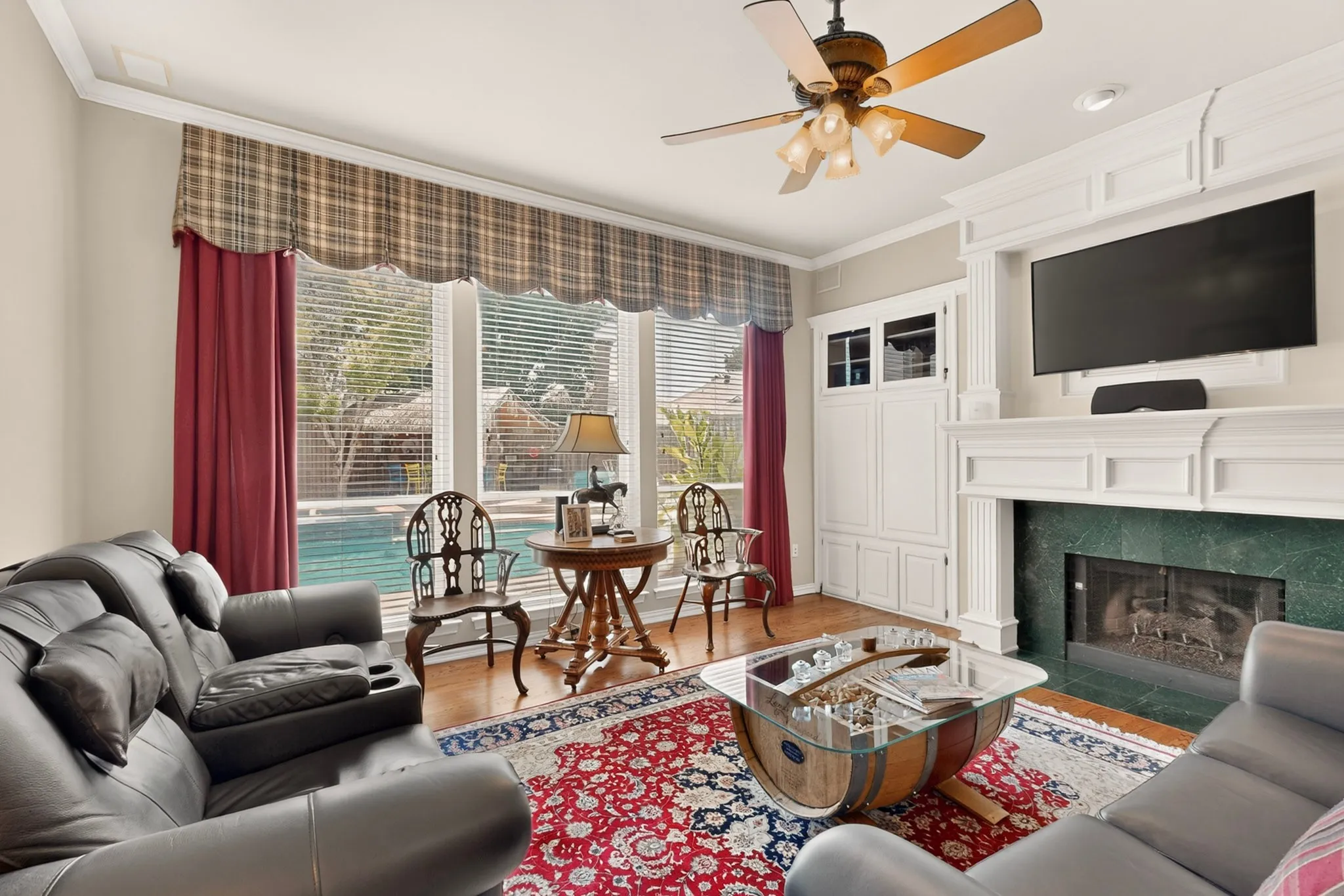 Hardwood flooring, custom built-in cabinetry, fireplace with a green stone surround, ceiling fan with integrated lighting, and crown molding