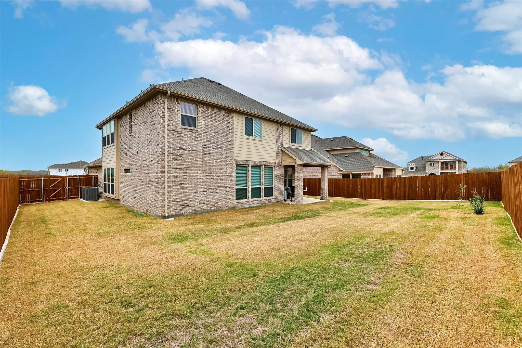 Expansive backyard with a full privacy fence, a covered patio, and a two-story exterior featuring brick and siding