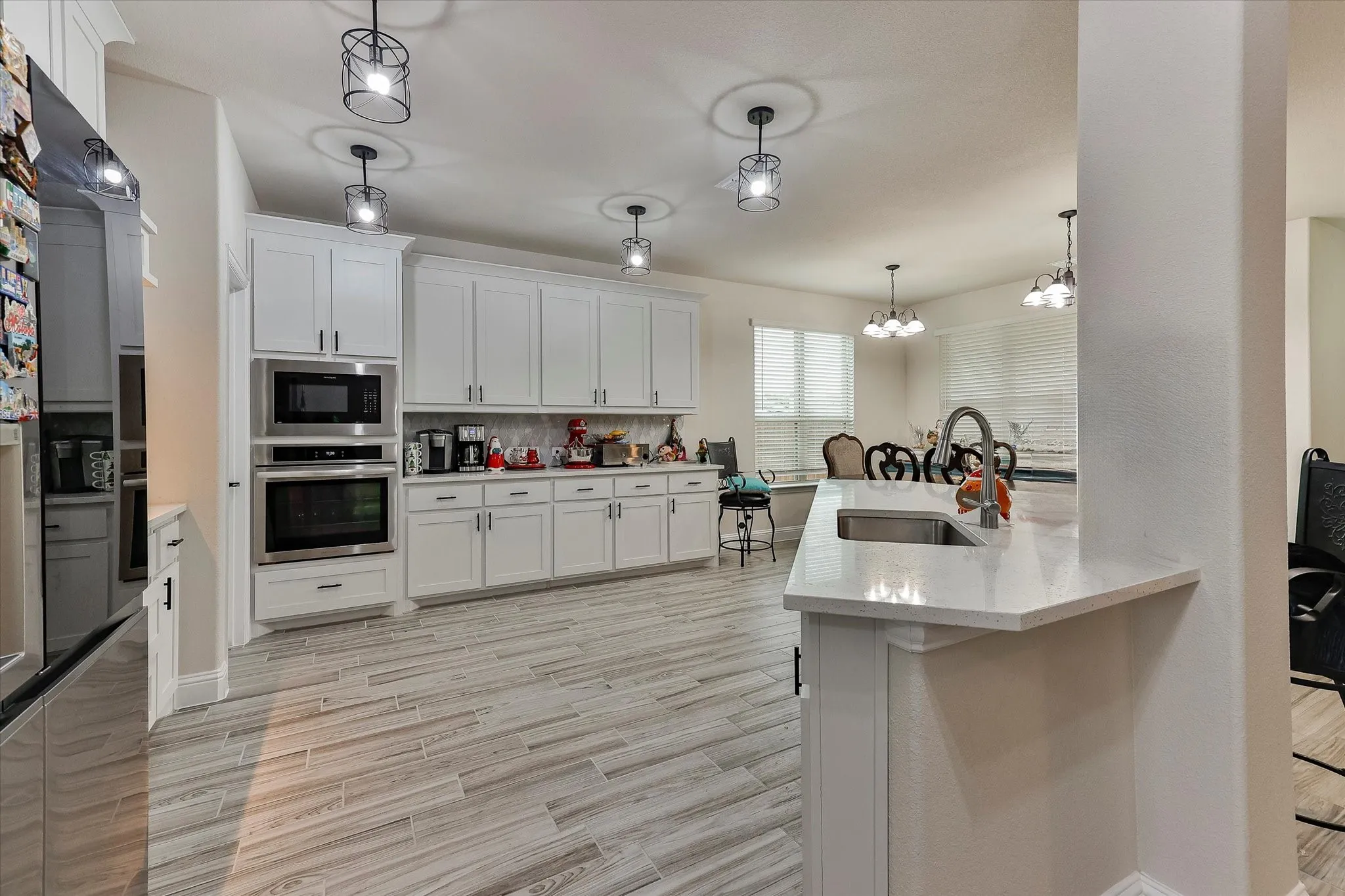 Kitchen with extensive white cabinetry, built-in stainless steel appliances, light-toned wood-finish flooring, and a kitchen island with an undermount sink