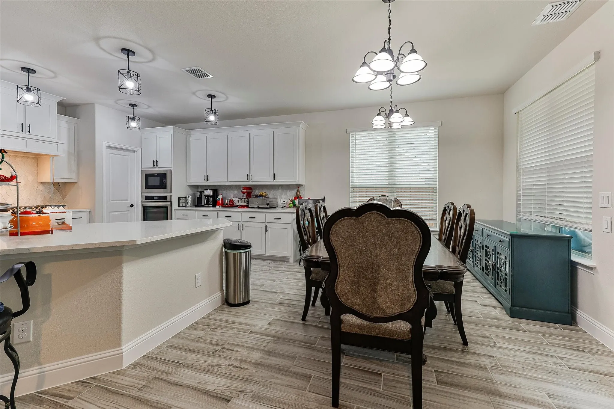 Open-concept living space featuring wood-finish flooring, white cabinetry, a kitchen island with a light-colored countertop, and a built-in oven and microwave