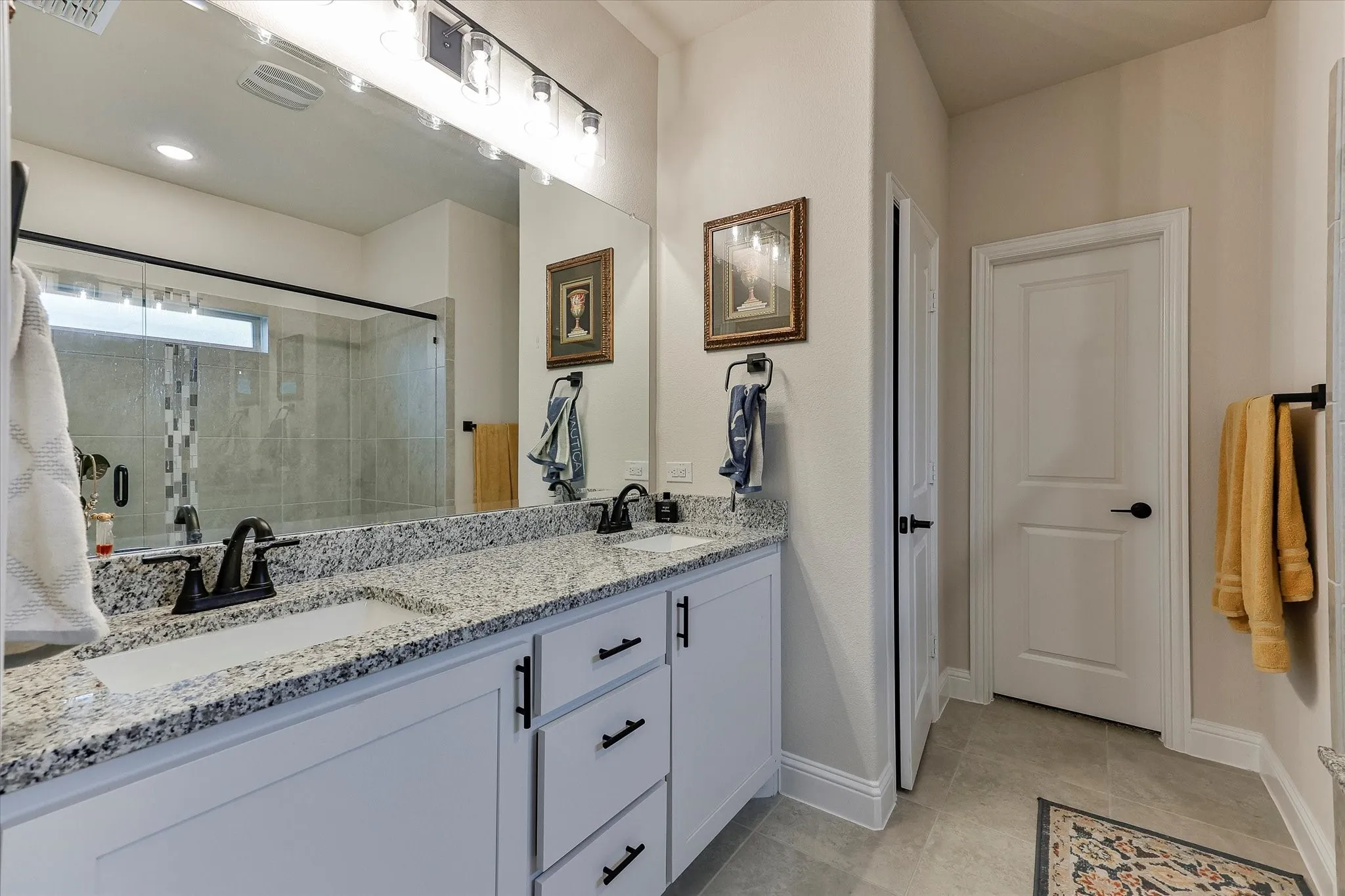 Dual vanity with integrated sinks, granite countertop, white cabinetry with black hardware, and an expansive wall mirror