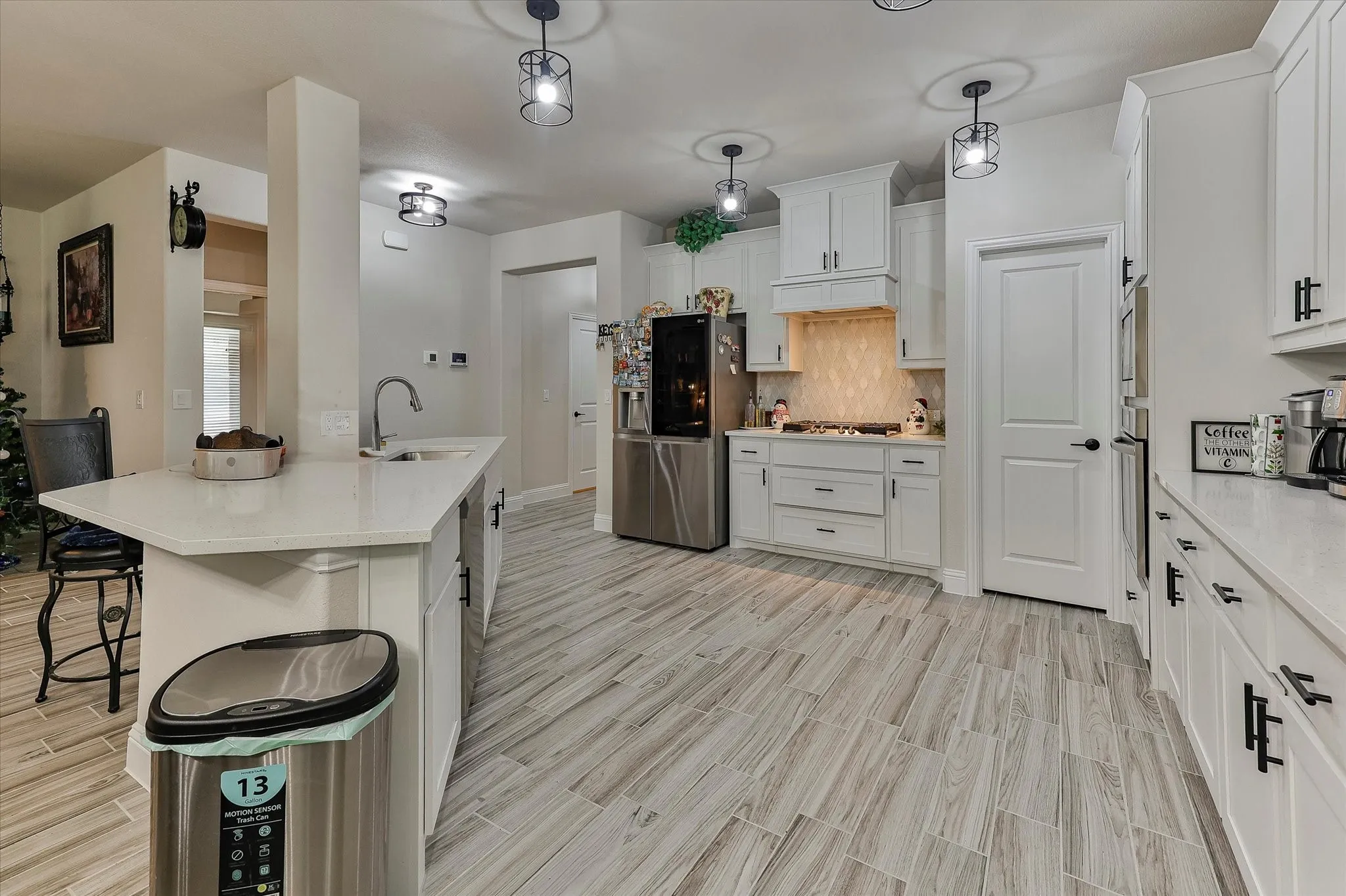 Kitchen featuring white cabinetry, light-toned countertops, a stainless steel refrigerator, a tile backsplash, and wood-finish flooring