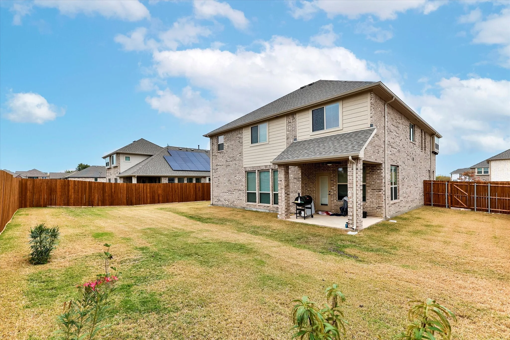 Spacious backyard featuring a covered patio, brick and siding exterior, and wood fencing