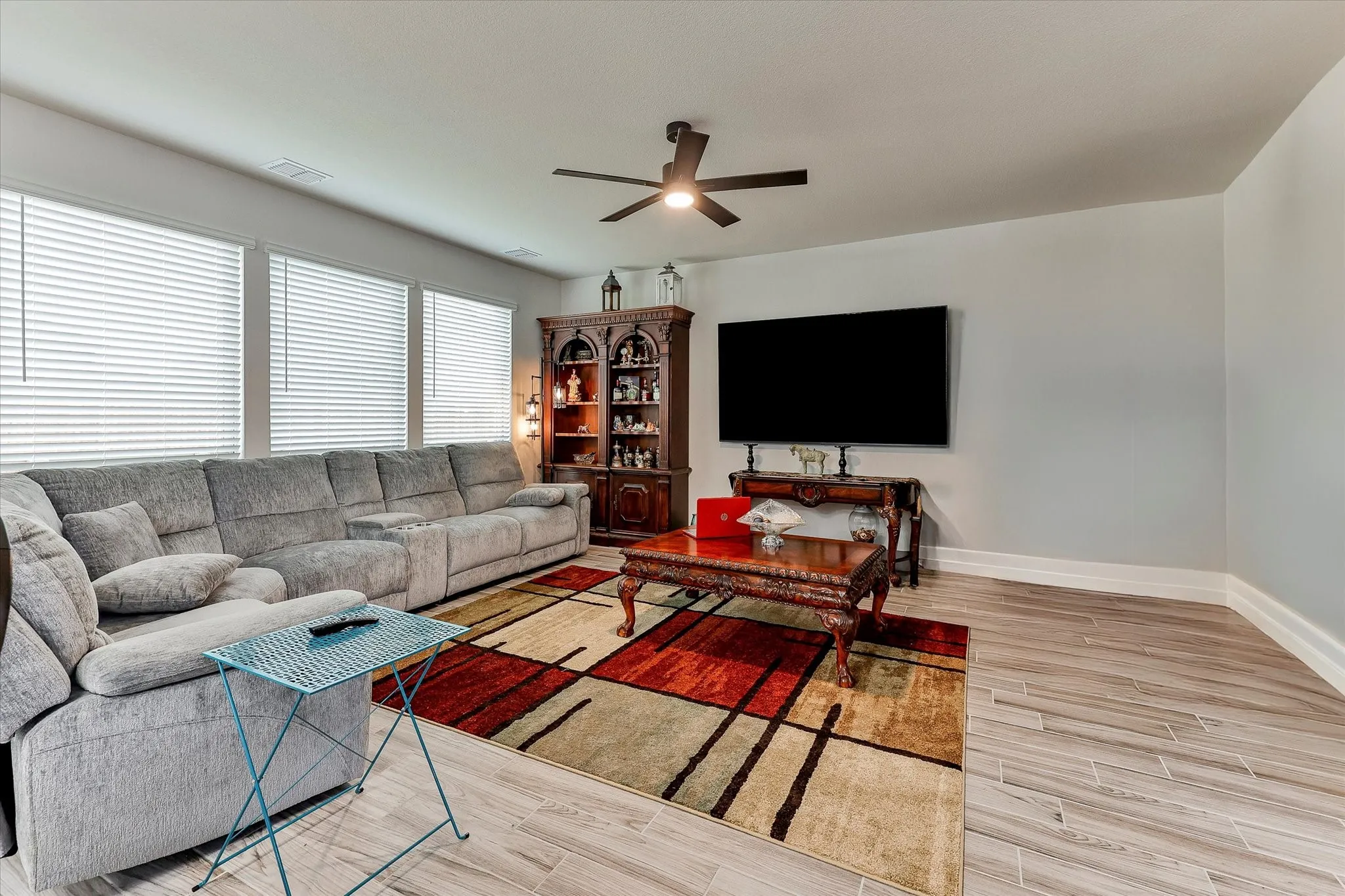 Wood-finish flooring, ceiling fan, multiple windows with blinds, recessed lighting, and wall-mounted television