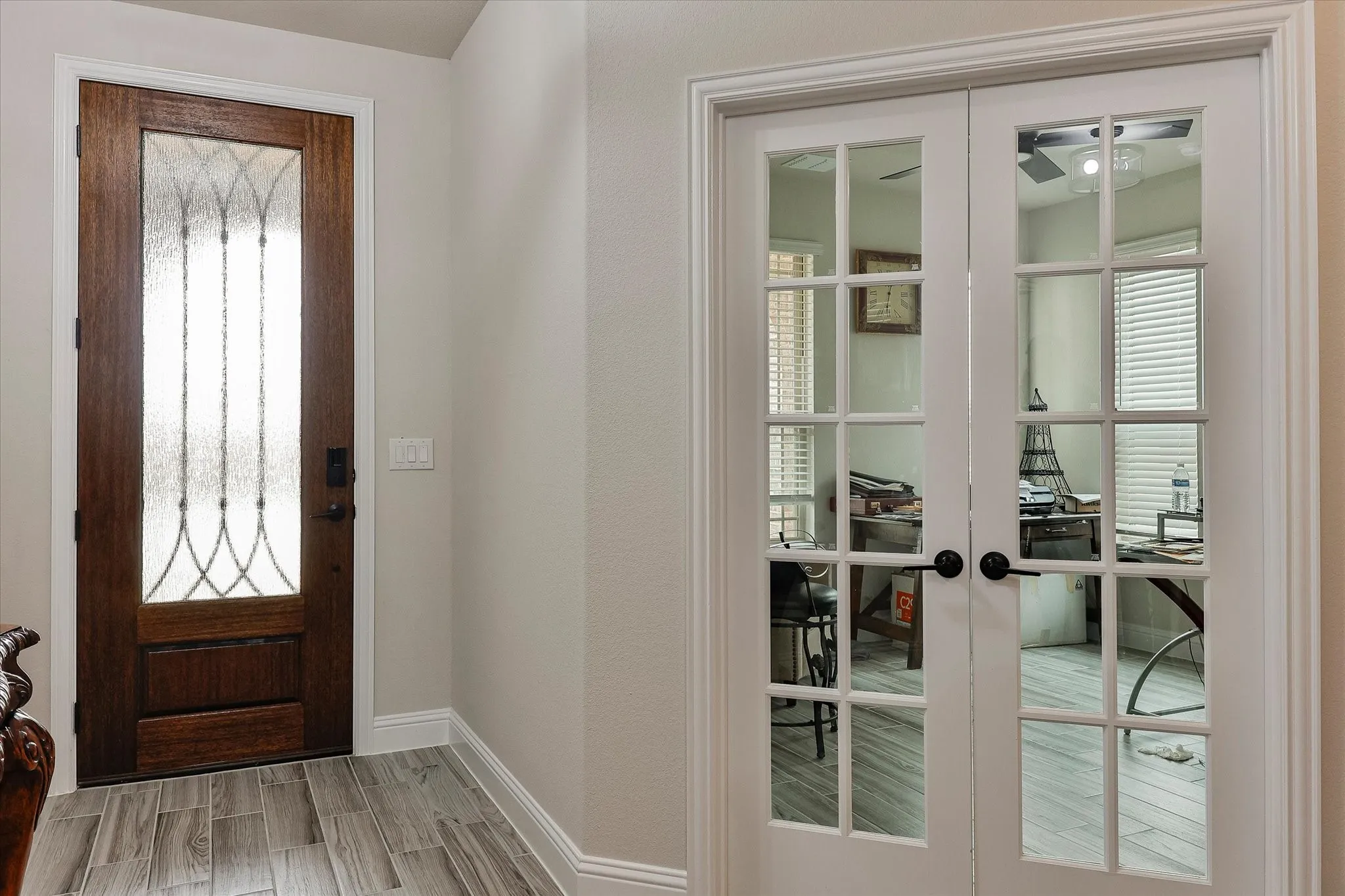 Wood-finish flooring, dark wood entry door with decorative glass, and white French doors with divided lites