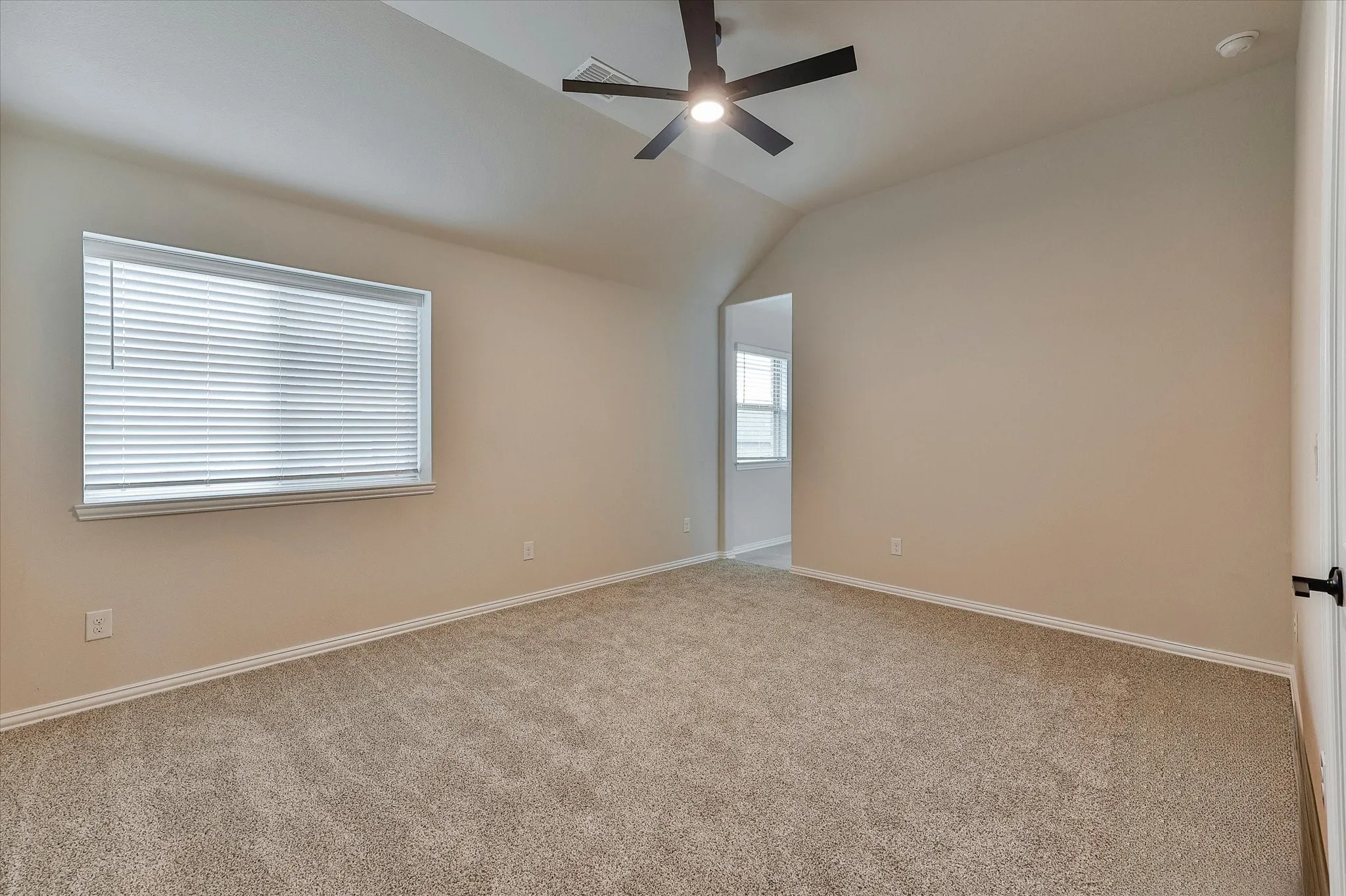 Sloped ceiling room featuring a ceiling fan with integrated lighting, a window with blinds, and neutral carpet flooring