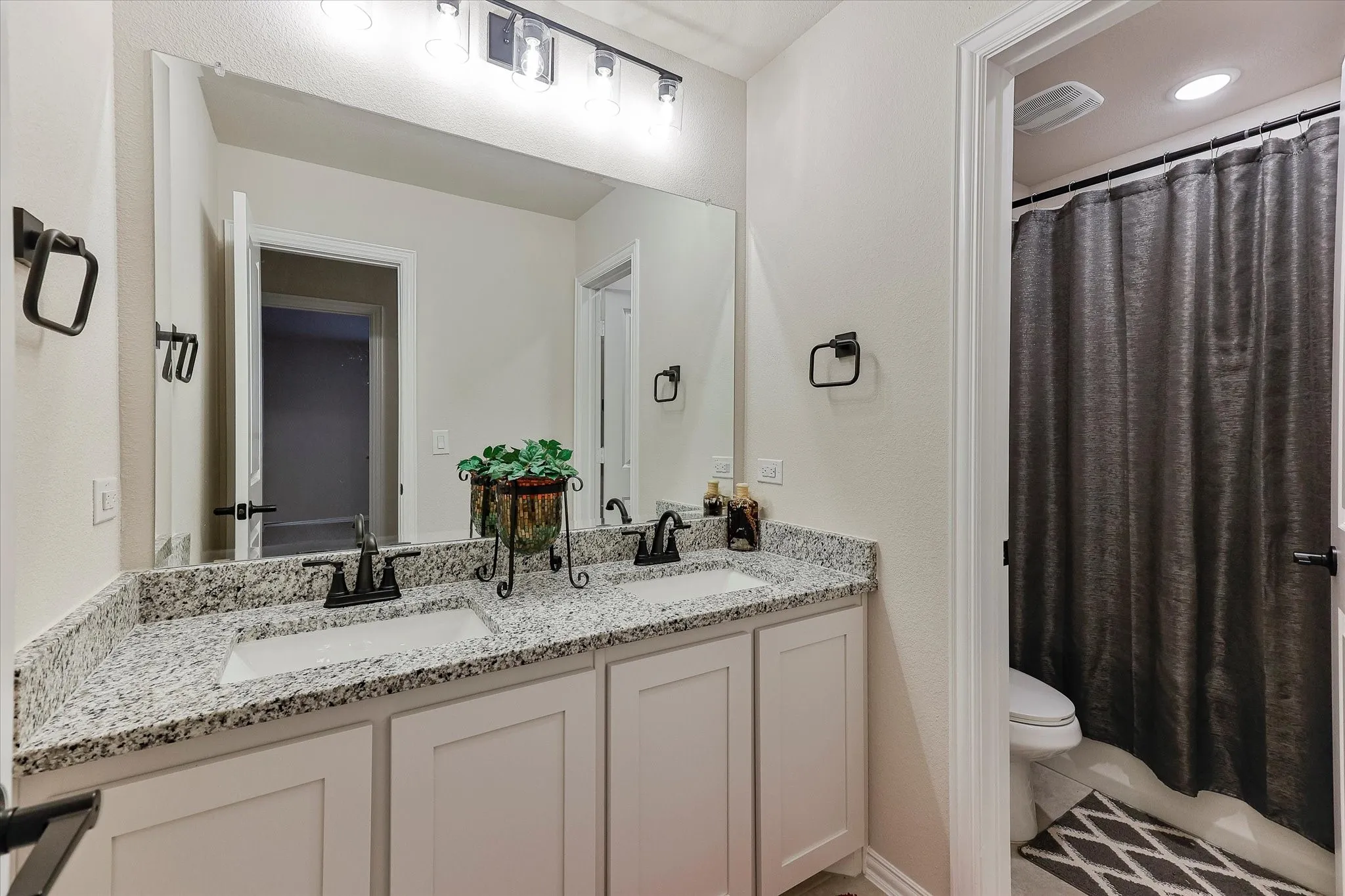 Dual vanity with granite countertop, white shaker-style cabinetry, and matte black hardware