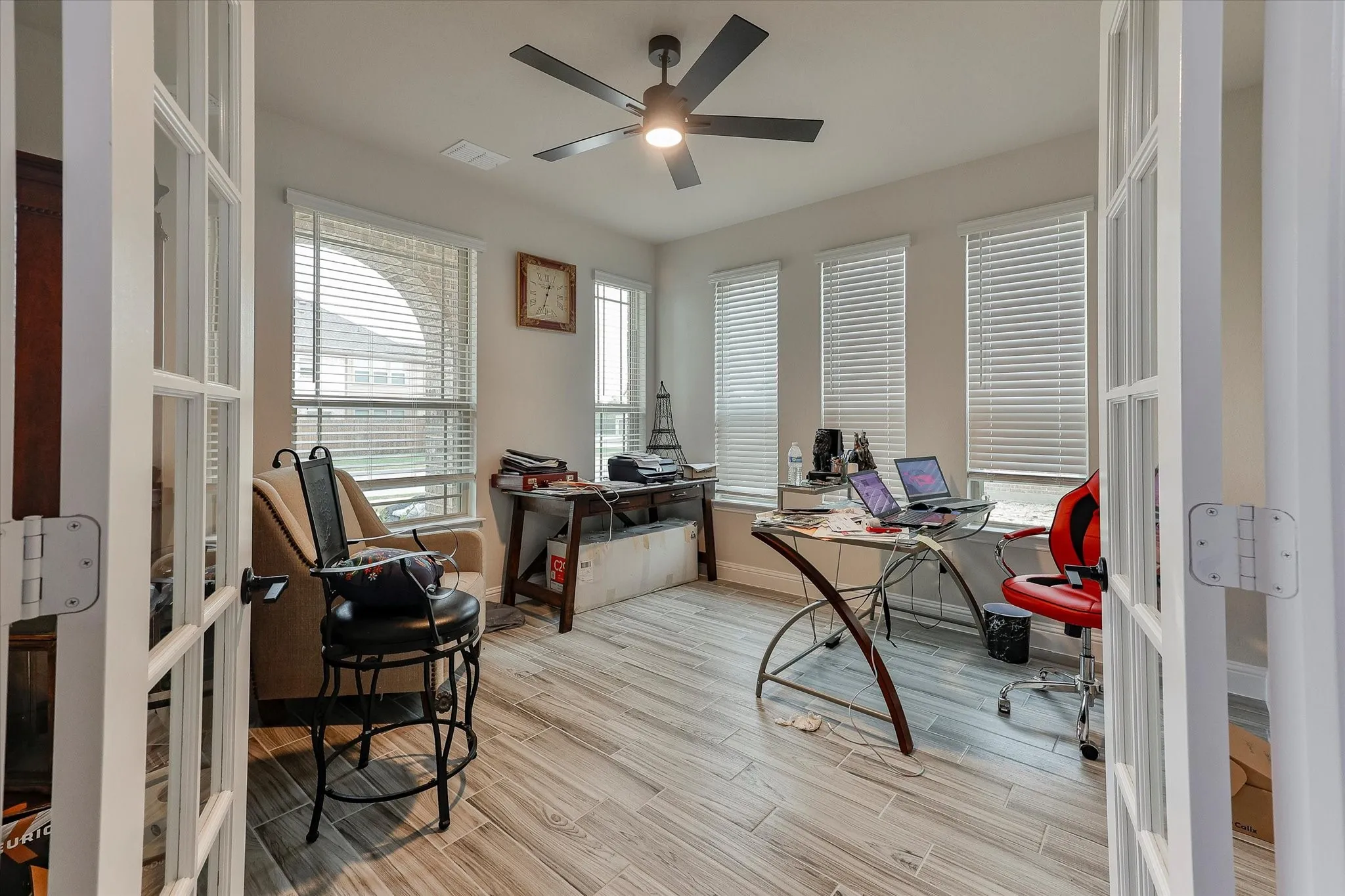 Room featuring French doors, wood-finish flooring, multiple windows with blinds, and a ceiling fan with integrated lighting