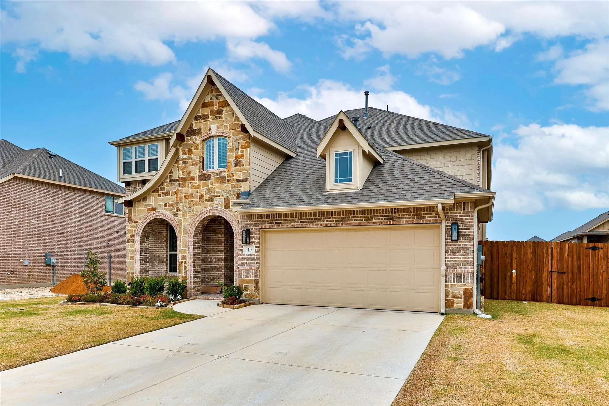Stone and brick exterior with arched entryway, two-car garage, dormer window, and shingle roofing