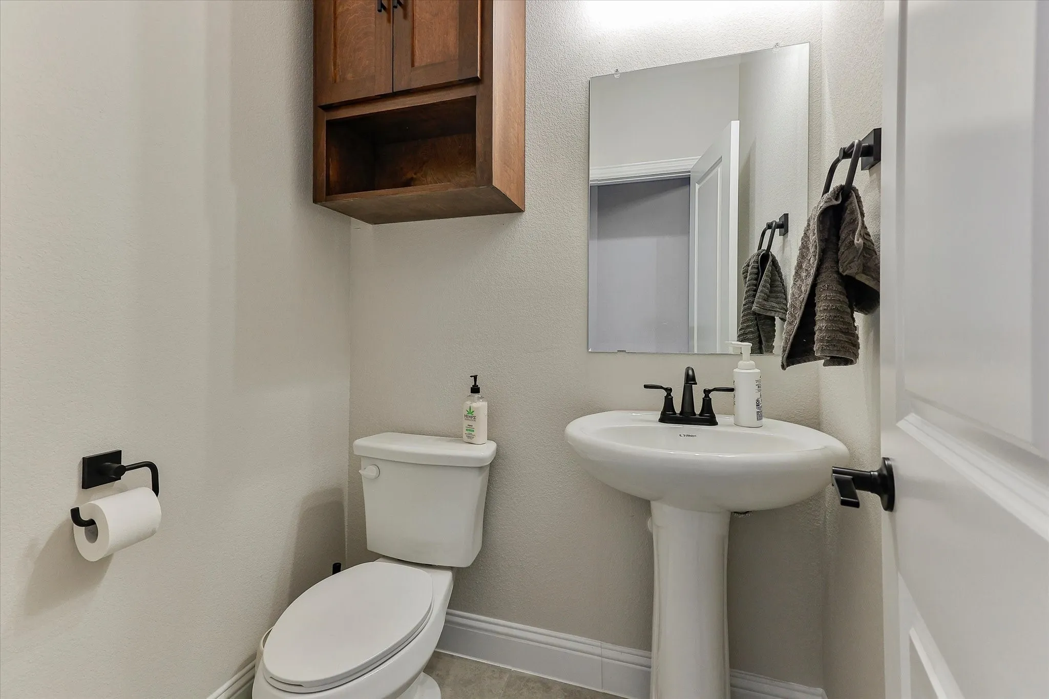 Pedestal sink with a matte black faucet, wall-mounted mirror, and white toilet