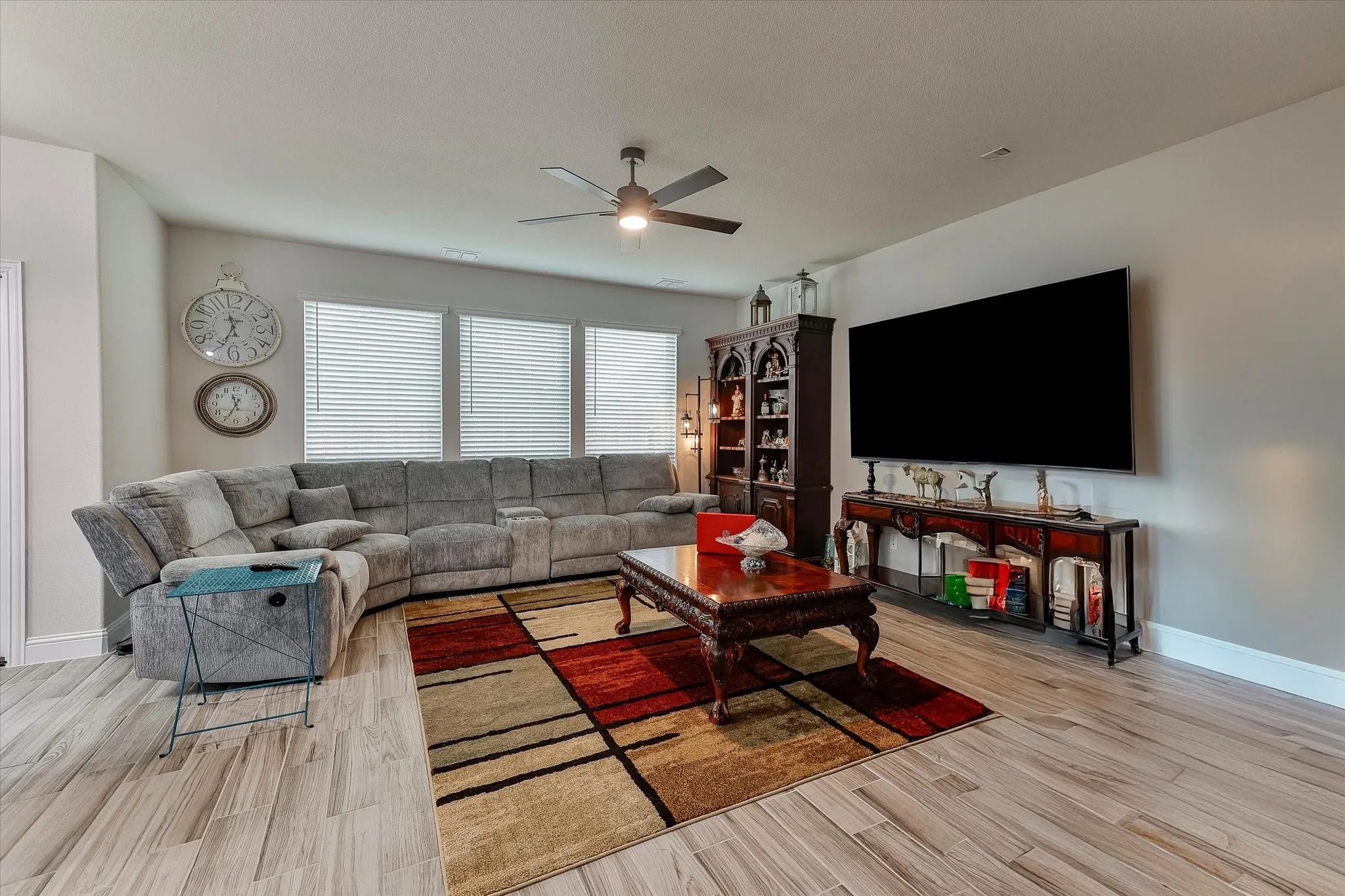 Spacious living area featuring wood-finish flooring, ample natural light from multiple windows, and a ceiling fan