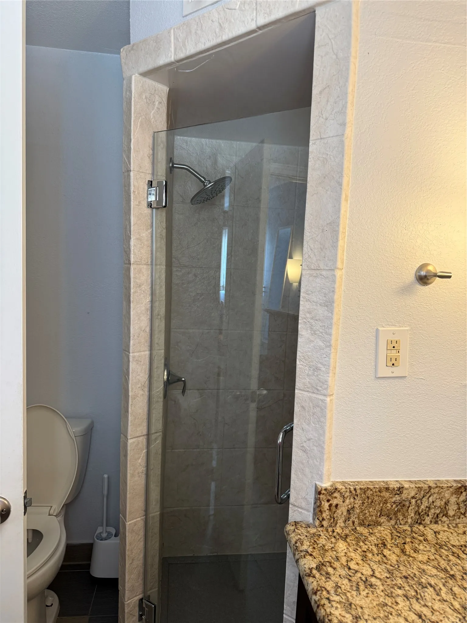 Glass-enclosed shower with a rainfall showerhead, complemented by a granite-finish countertop and contemporary vanity lighting