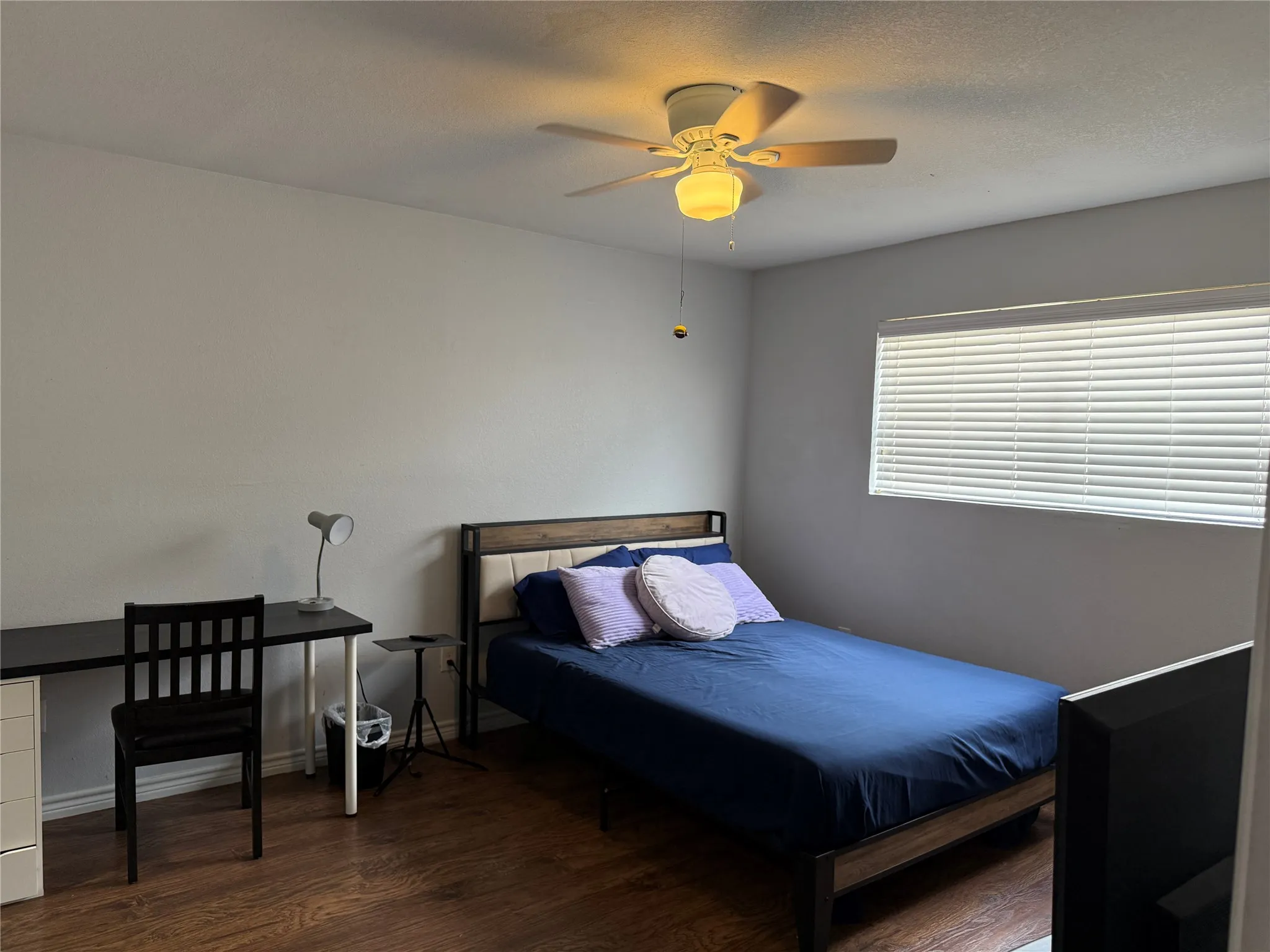 Bedroom featuring wood-finish flooring, a ceiling fan with integrated lighting, and a window with horizontal blinds