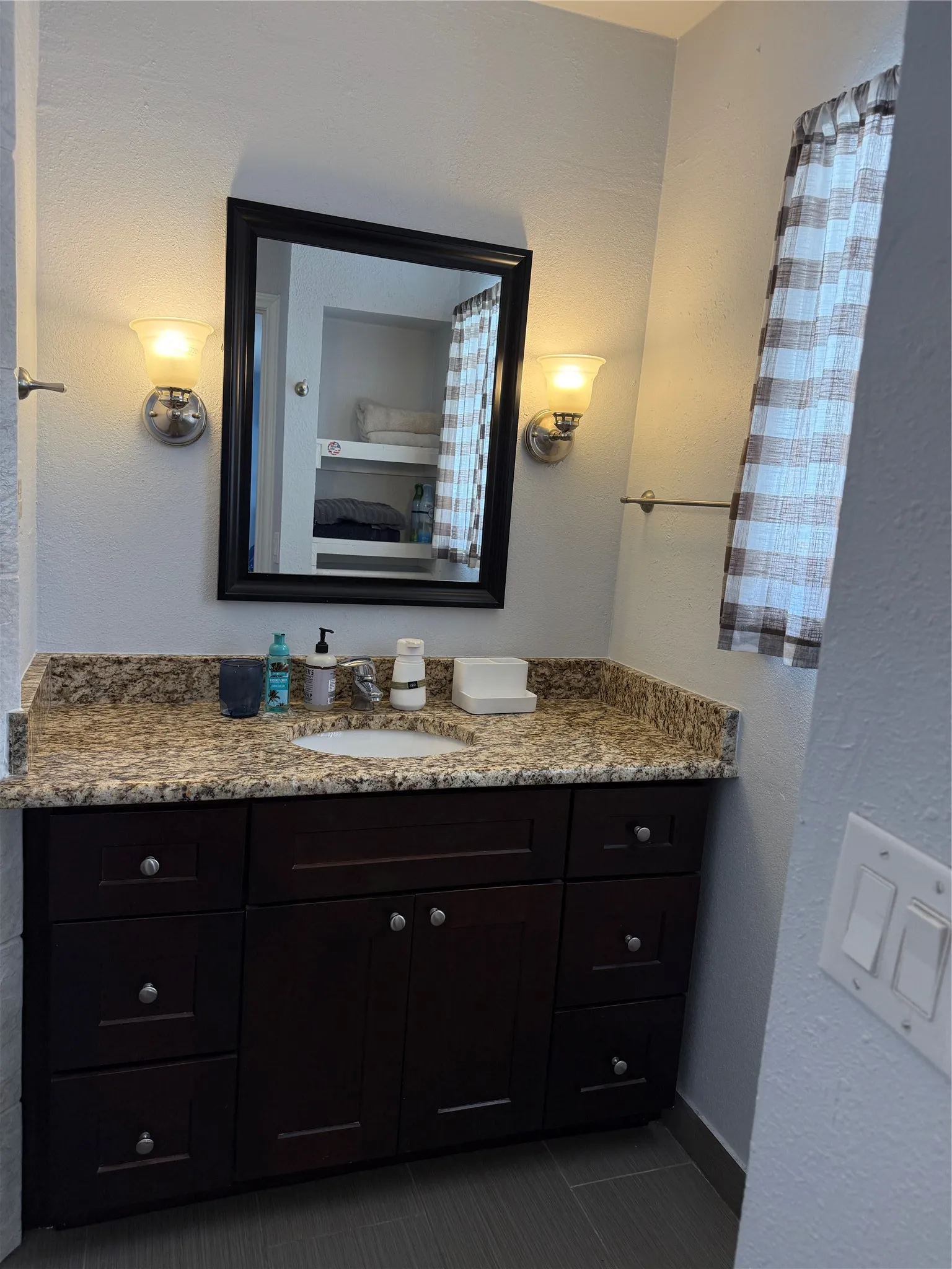 Bathroom vanity featuring a granite-style countertop with an undermount sink, dark wood-finish cabinetry, and a framed mirror