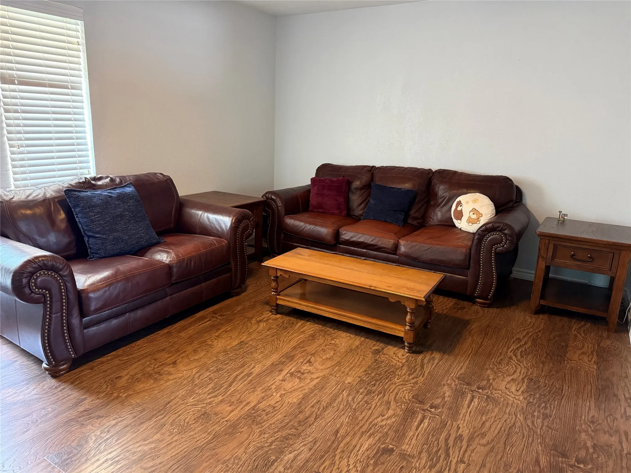 Spacious room featuring wood-finish flooring, white walls, and a window with horizontal blinds