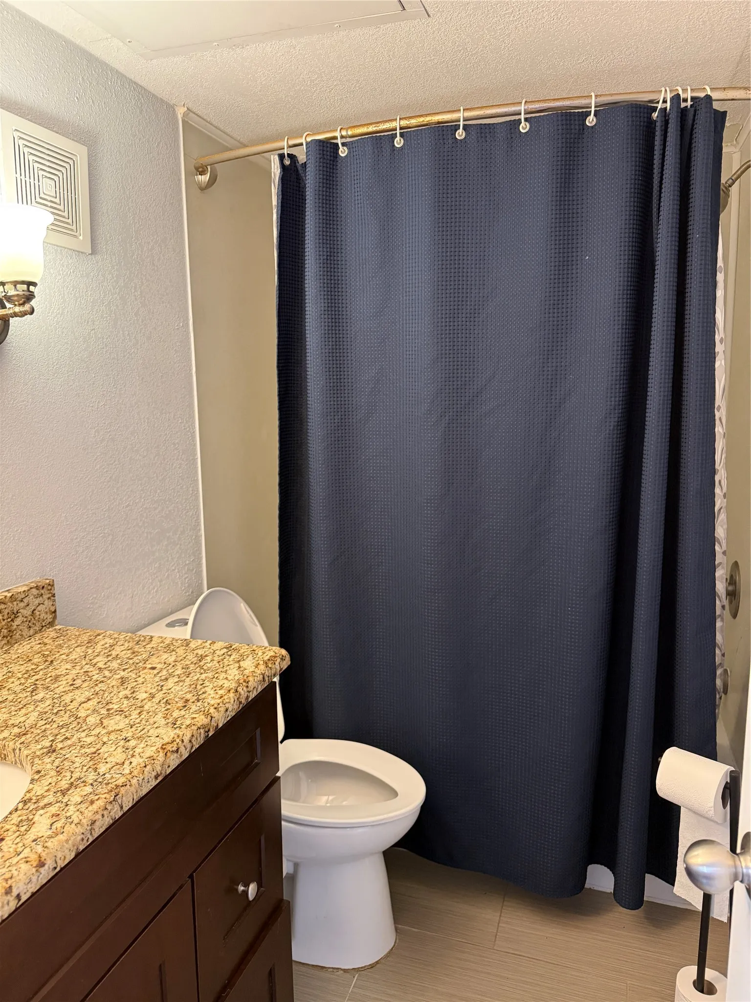 Bathroom featuring a granite countertop vanity, wood-finish cabinetry, a white toilet, and a shower with a curved rod