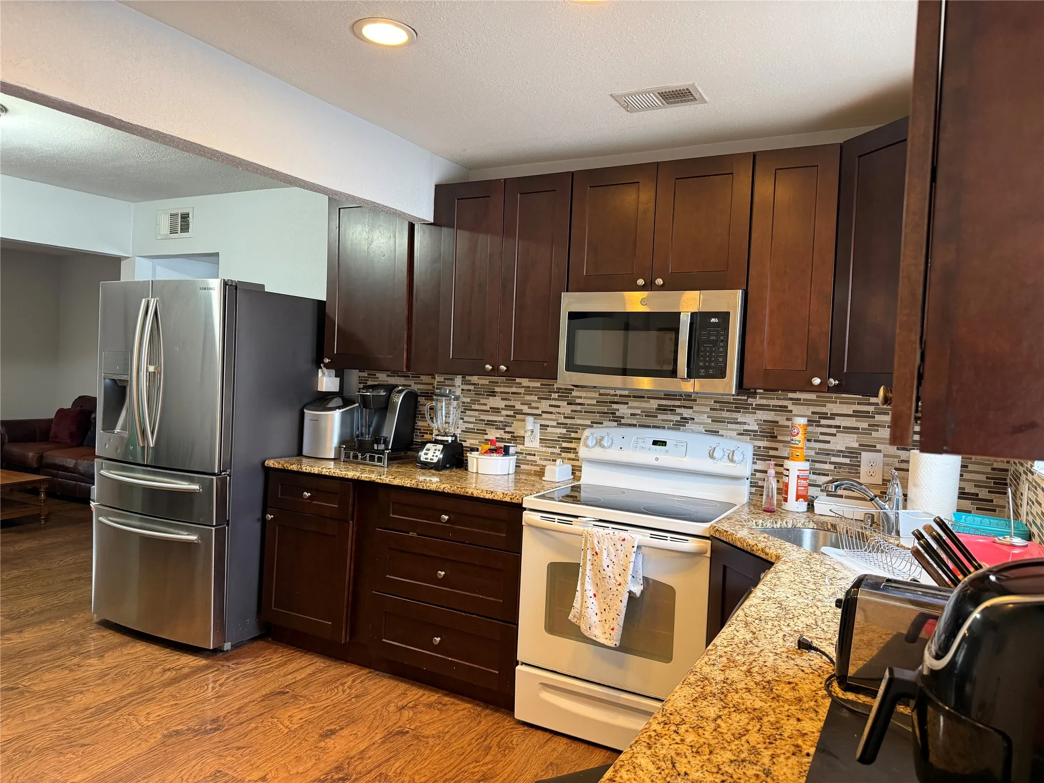Kitchen featuring wood-finish flooring, dark wood cabinetry, granite-style countertops, mosaic tile backsplash, and recessed lighting