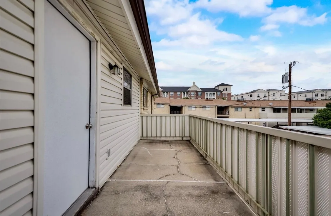 Outdoor balcony with a solid railing, concrete flooring, and an exterior light fixture