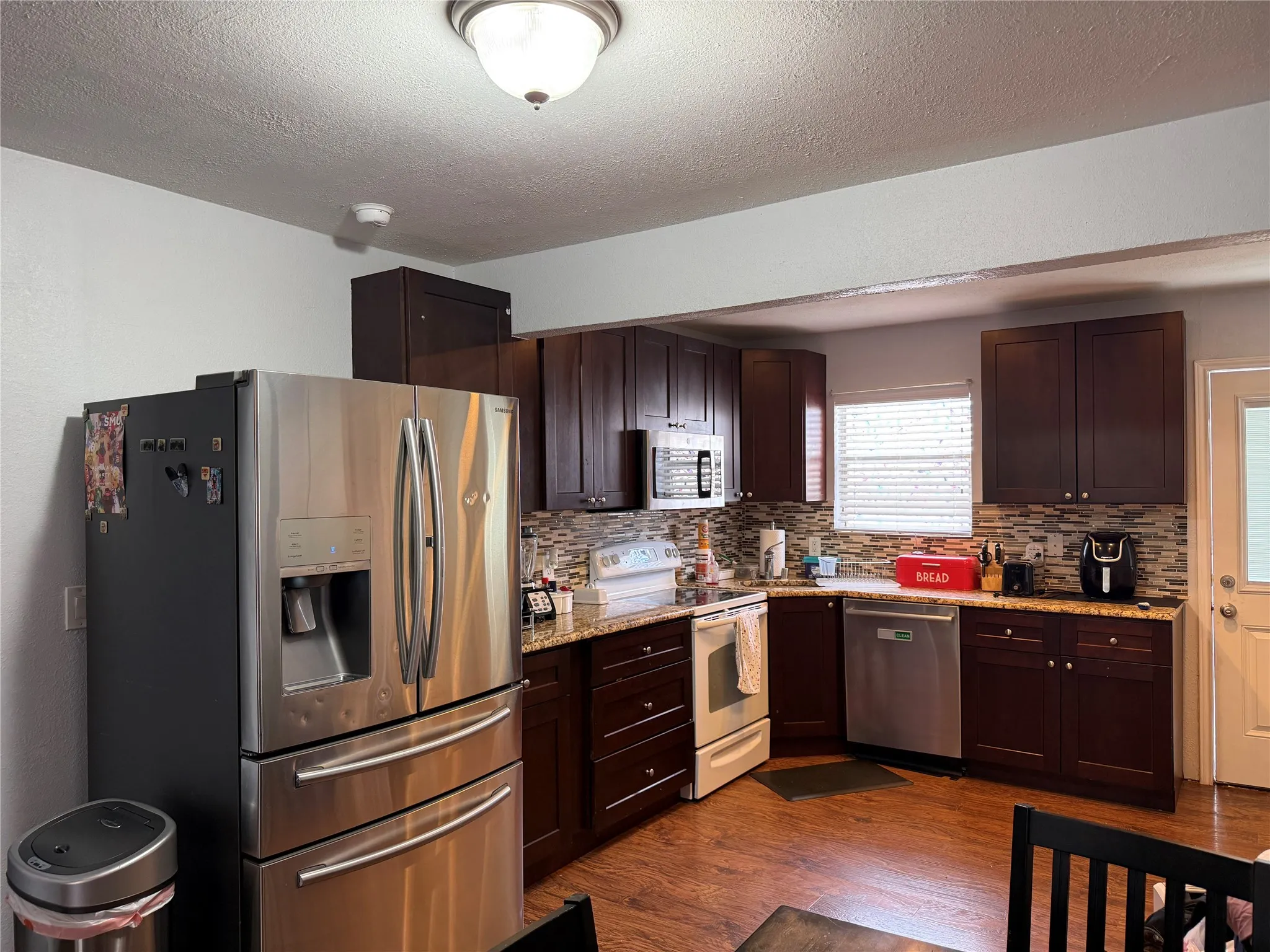 Kitchen featuring dark wood-finish cabinetry, granite-style countertops, and a mosaic tile backsplash