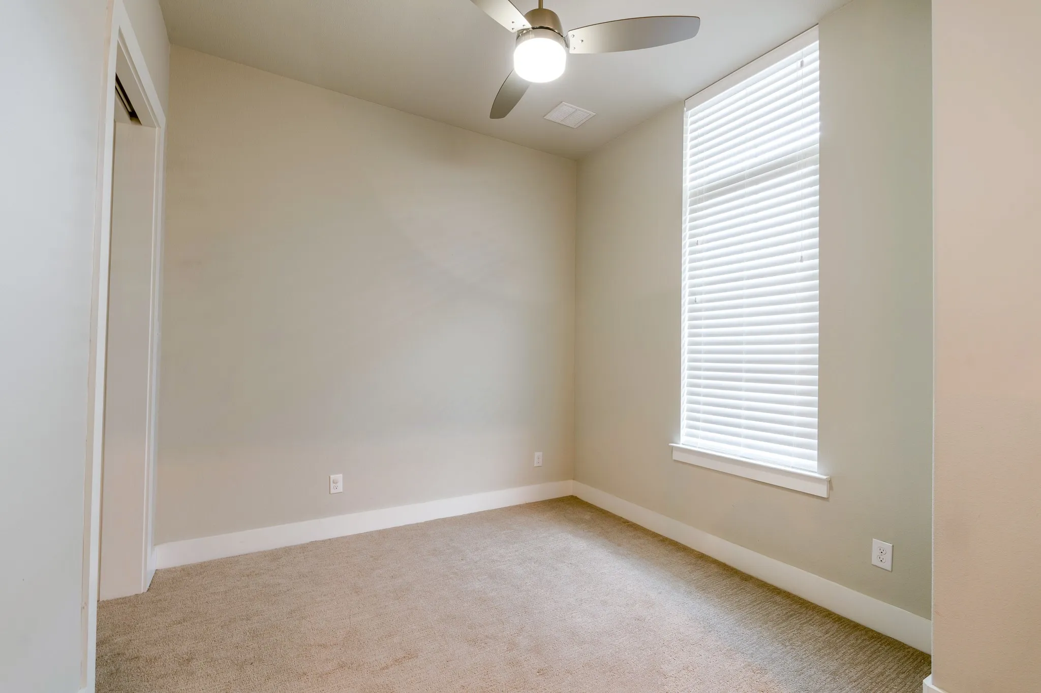 Third floor bedroom: Neutral-toned room featuring a tall window with white blinds, carpet flooring, a ceiling fan with integrated lighting, and white baseboards