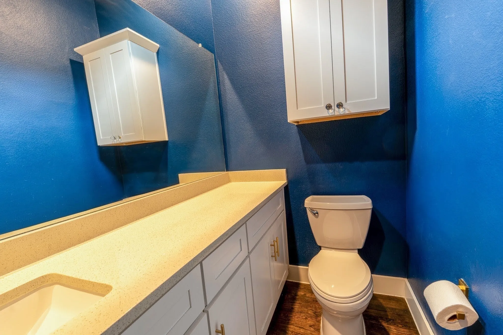 2nd Floor half-bathroom featuring a vanity with an integrated sink, quartz countertop, a full-width mirror, white cabinetry, a wall-mounted storage cabinet, and wood-finish flooring
