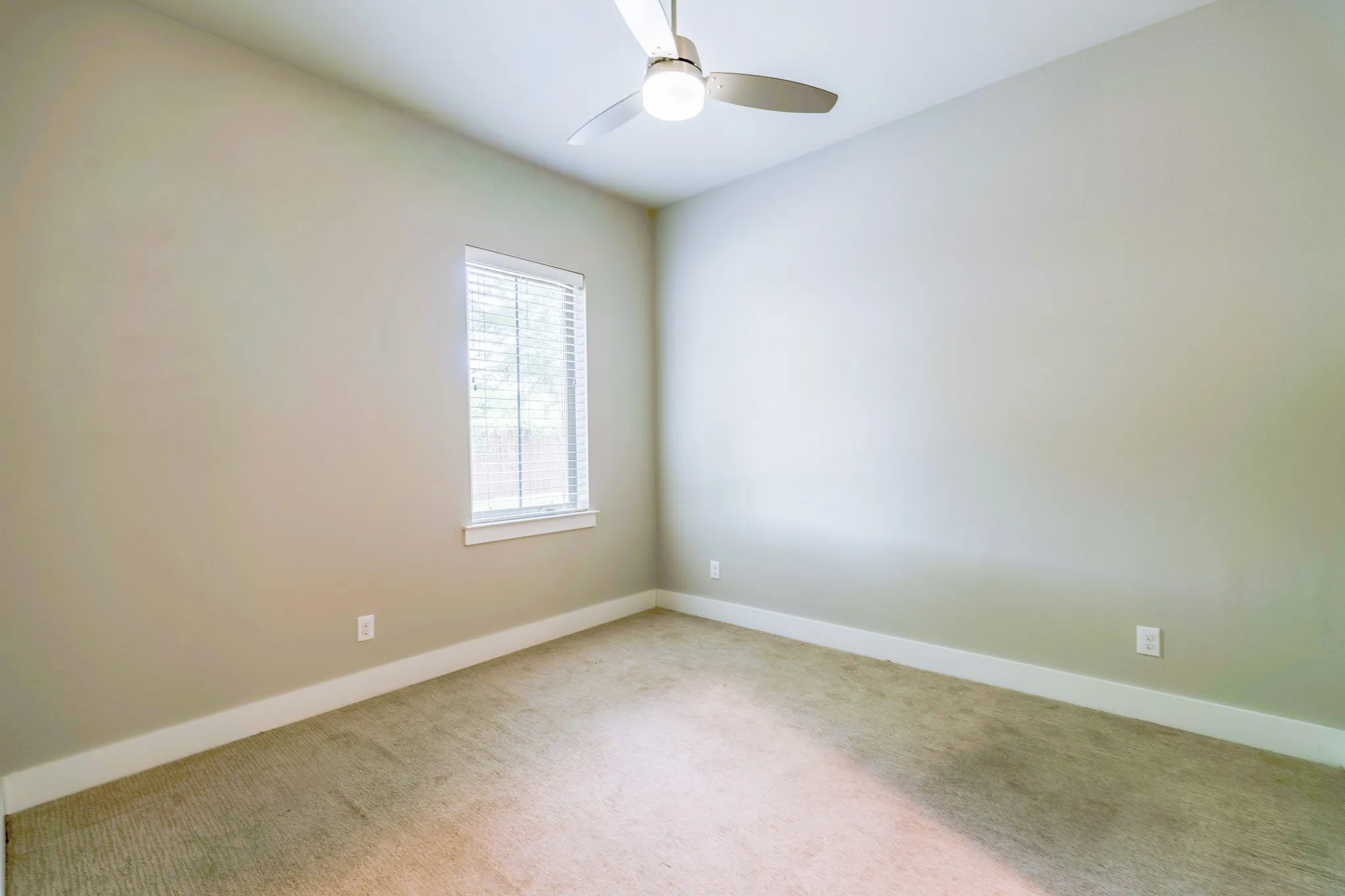 Neutral-toned room featuring a single window with blinds, a ceiling fan with integrated lighting, and light-colored carpeting