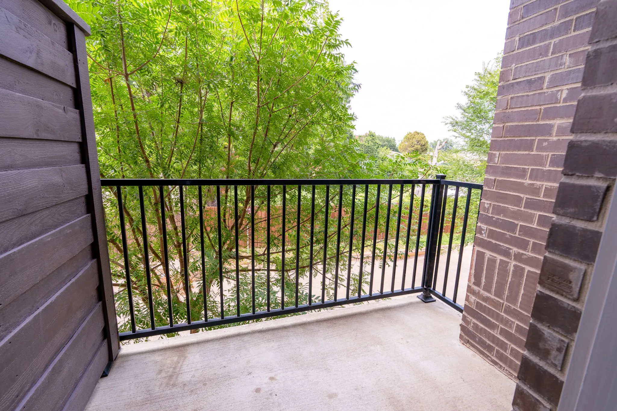 2nd floor outdoor balcony featuring concrete flooring, black metal railing, and a brick exterior wall