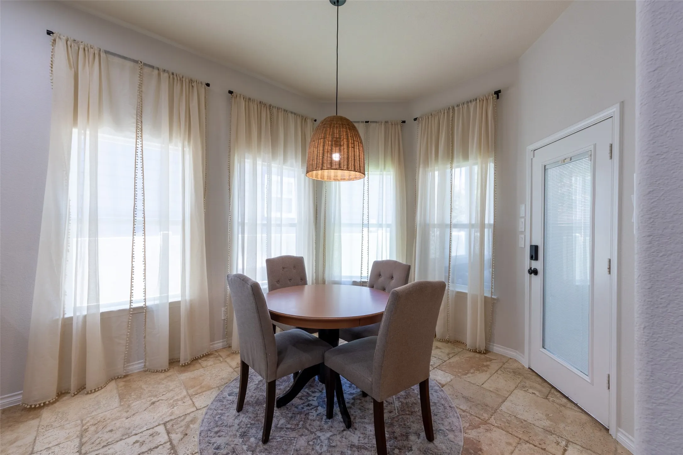 Bay window with sheer window treatments, woven pendant light fixture, and tile flooring