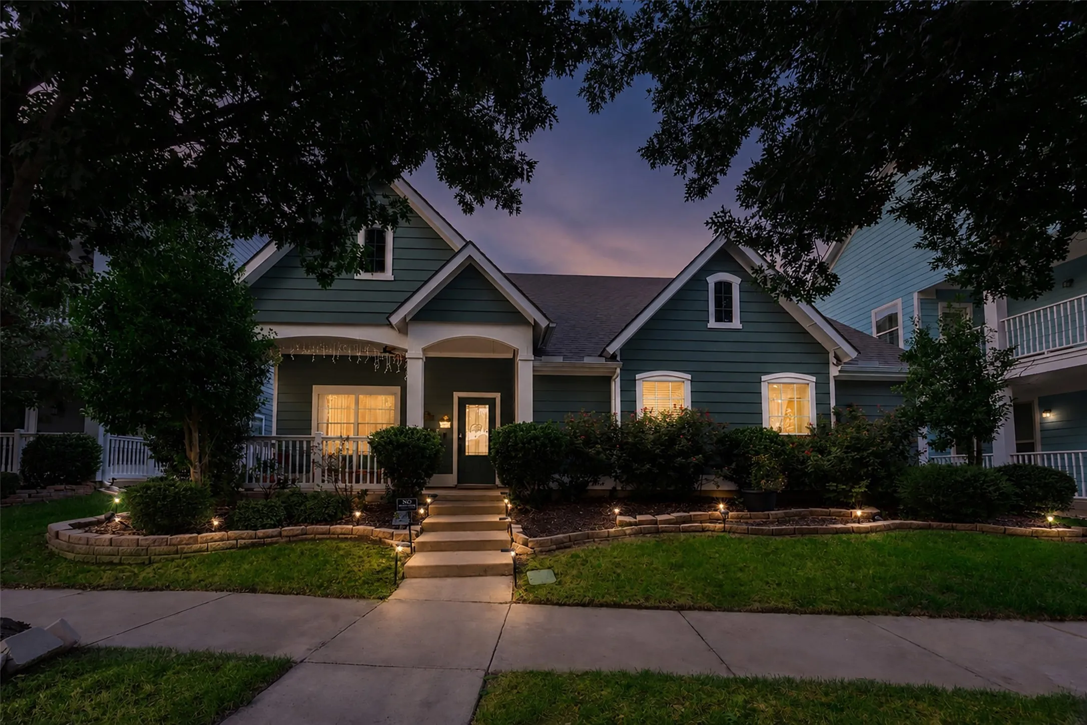 Siding exterior with dormer window accents, covered front porch, concrete pathway, stone-faced landscape beds, and established landscaping