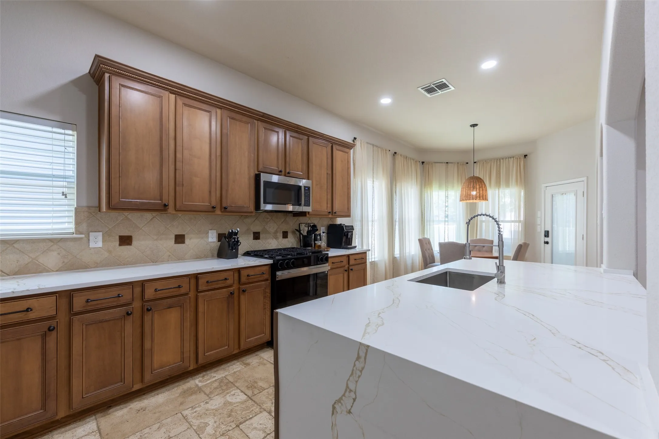 Kitchen featuring wood cabinetry, stainless steel appliances, a tile backsplash, light-toned countertops, and an island with an undermount sink