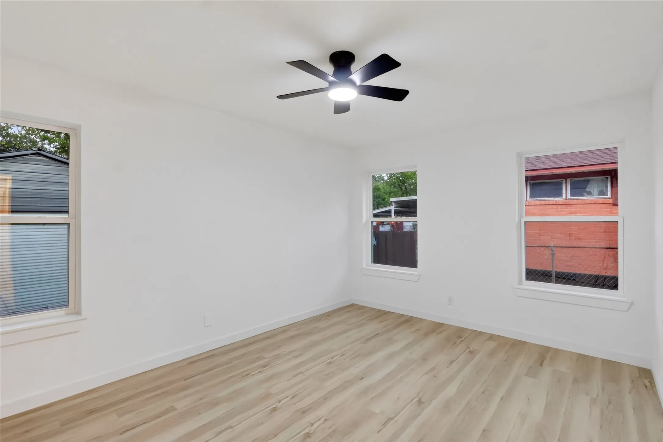 Third Bedroom: White walls, wood-finish flooring, three windows, and a ceiling fan with integrated lighting