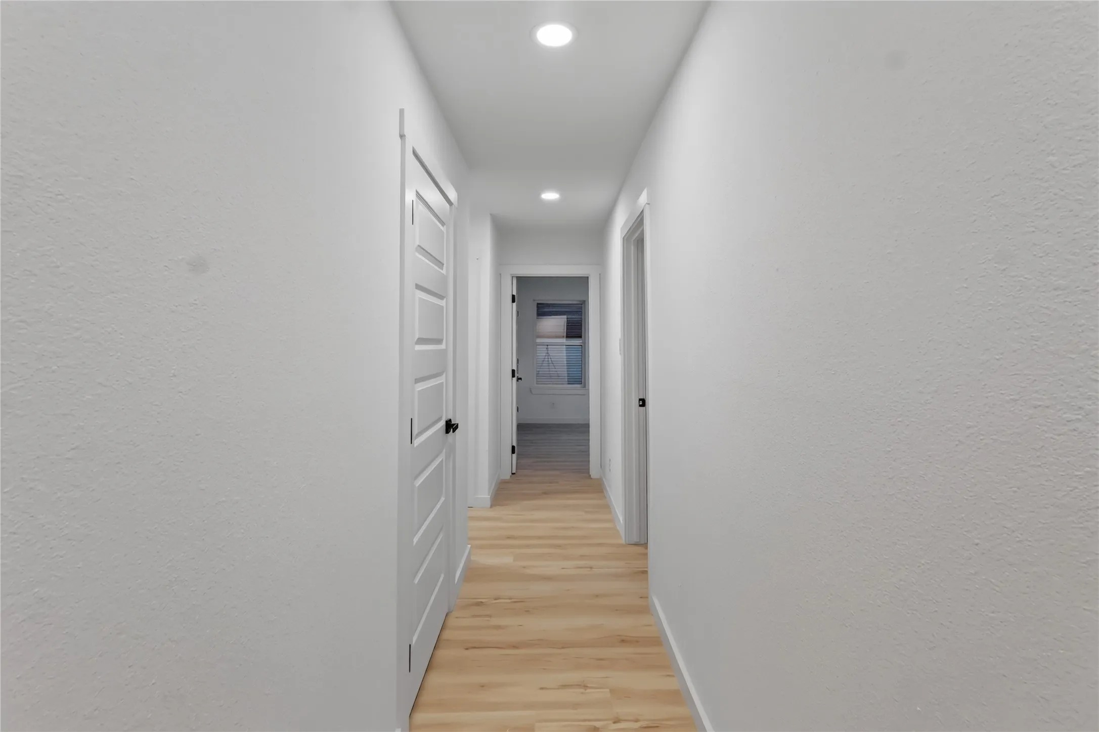 Recessed lighting illuminates the hallway with wood-finish flooring and solid panel doors