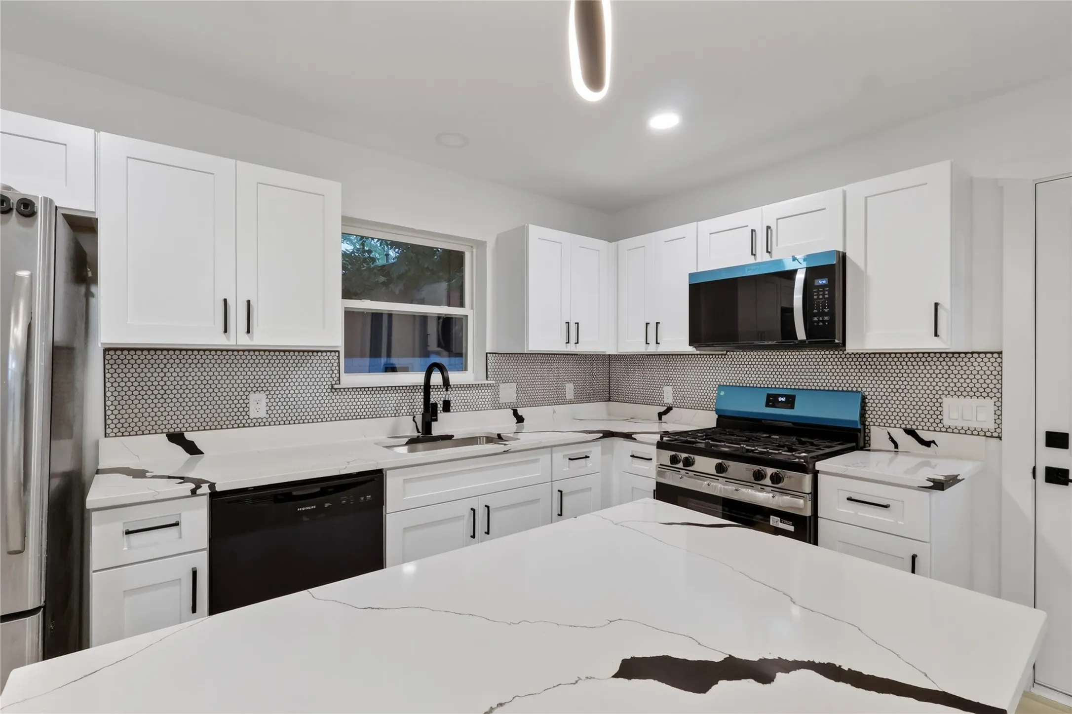Modern kitchen featuring white shaker-style cabinetry, a spacious center island with a stone countertop, a tile backsplash, stainless steel appliances, and a black sink with a matte black faucet